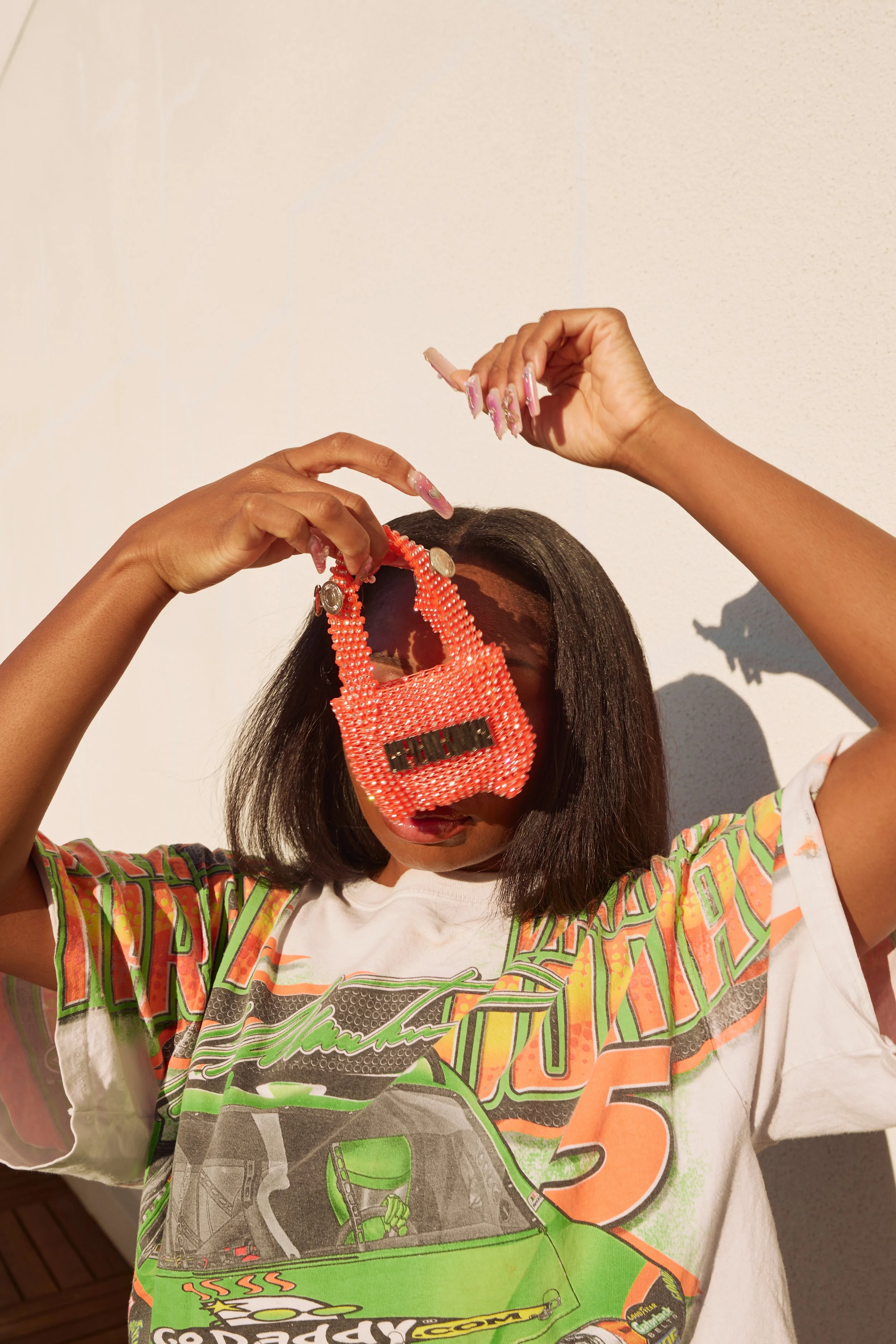 Model holding the Cheyennekimora orange mini bag in front of her face, the bag swinging mid-motion.
