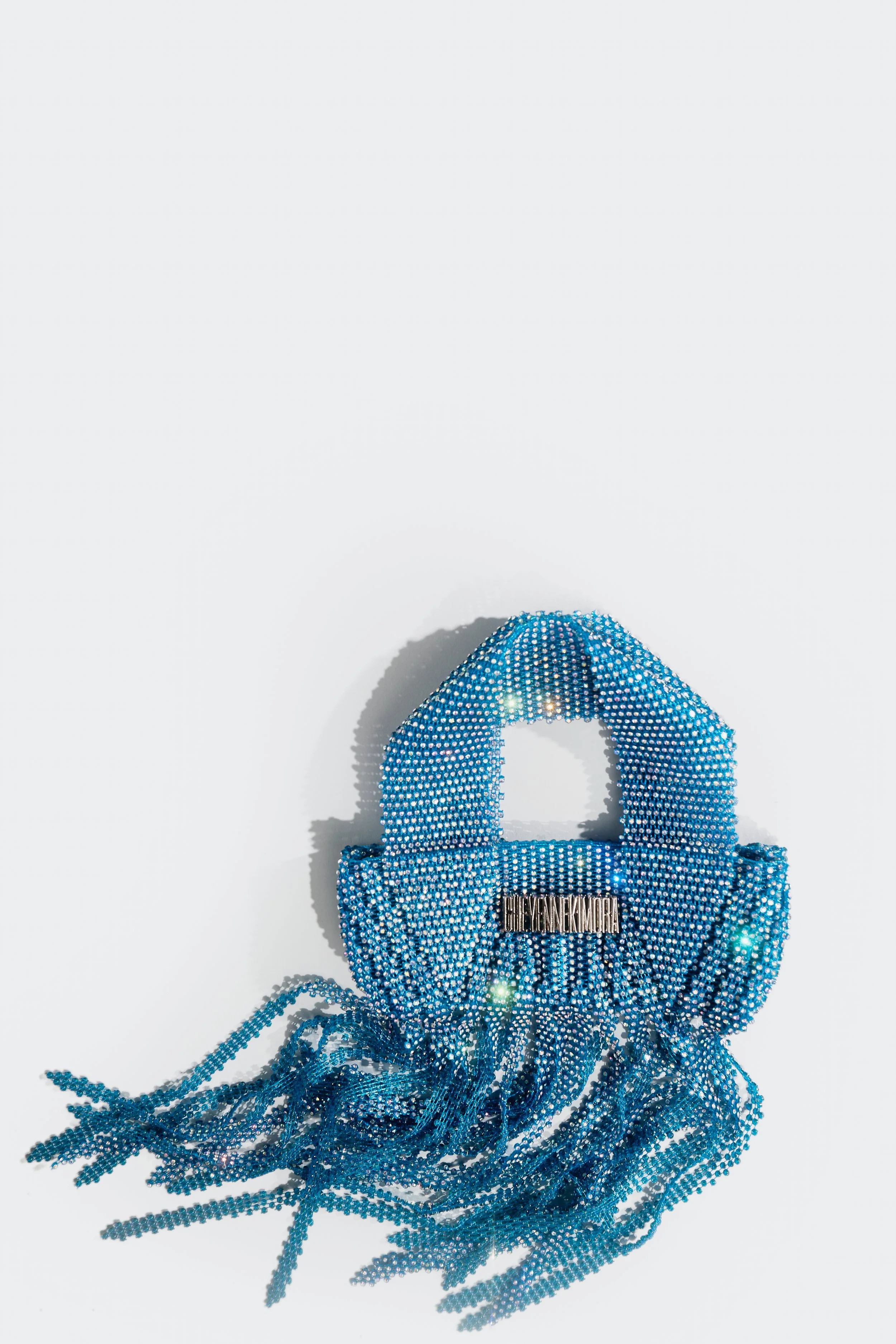 A blue handbag adorned with crystals, featuring fringe at the bottom, against a white background.