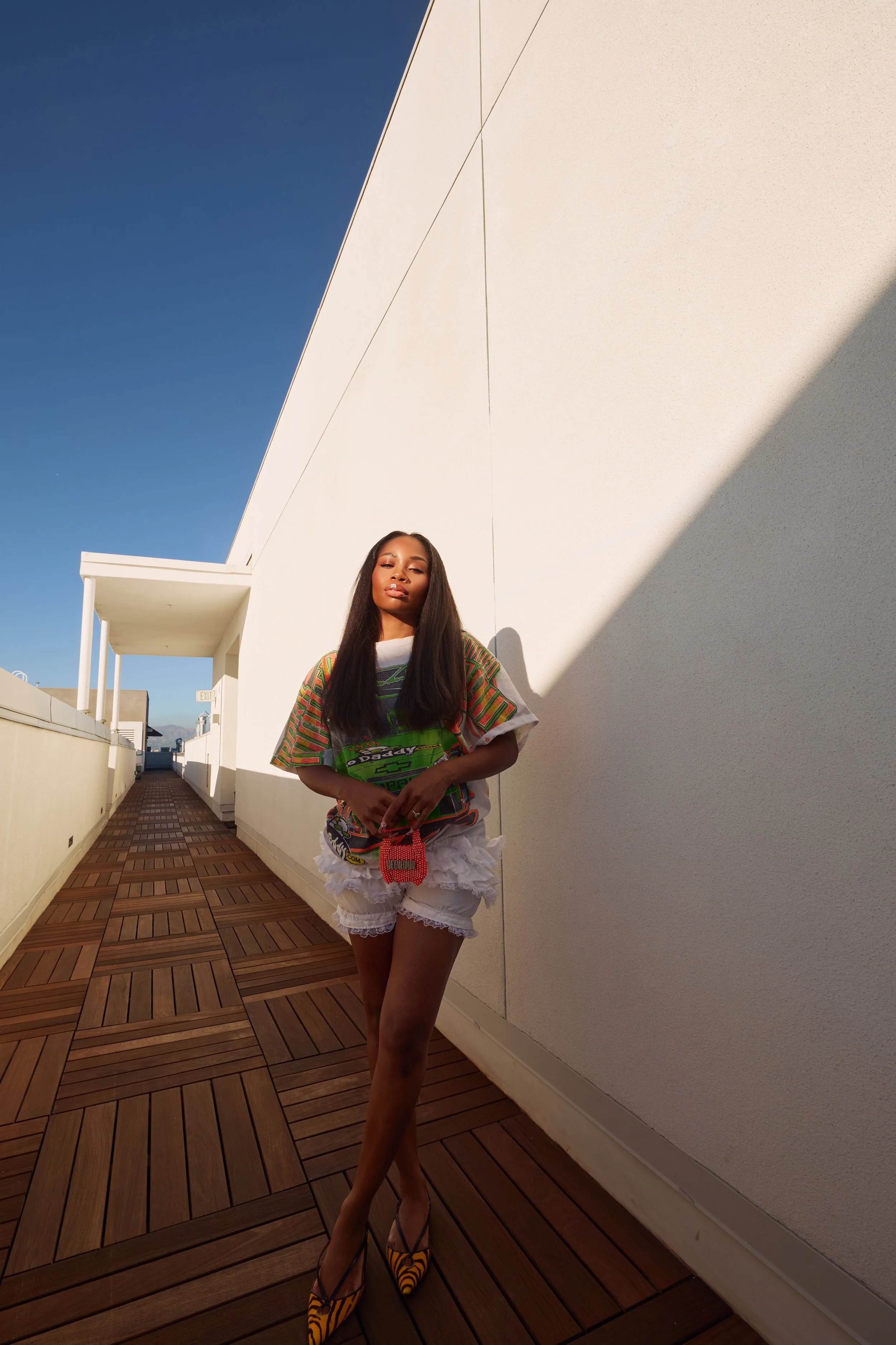 Full-body straight-on shot of the model with legs crossed, holding the Cheyennekimora orange mini bag at her waist.
