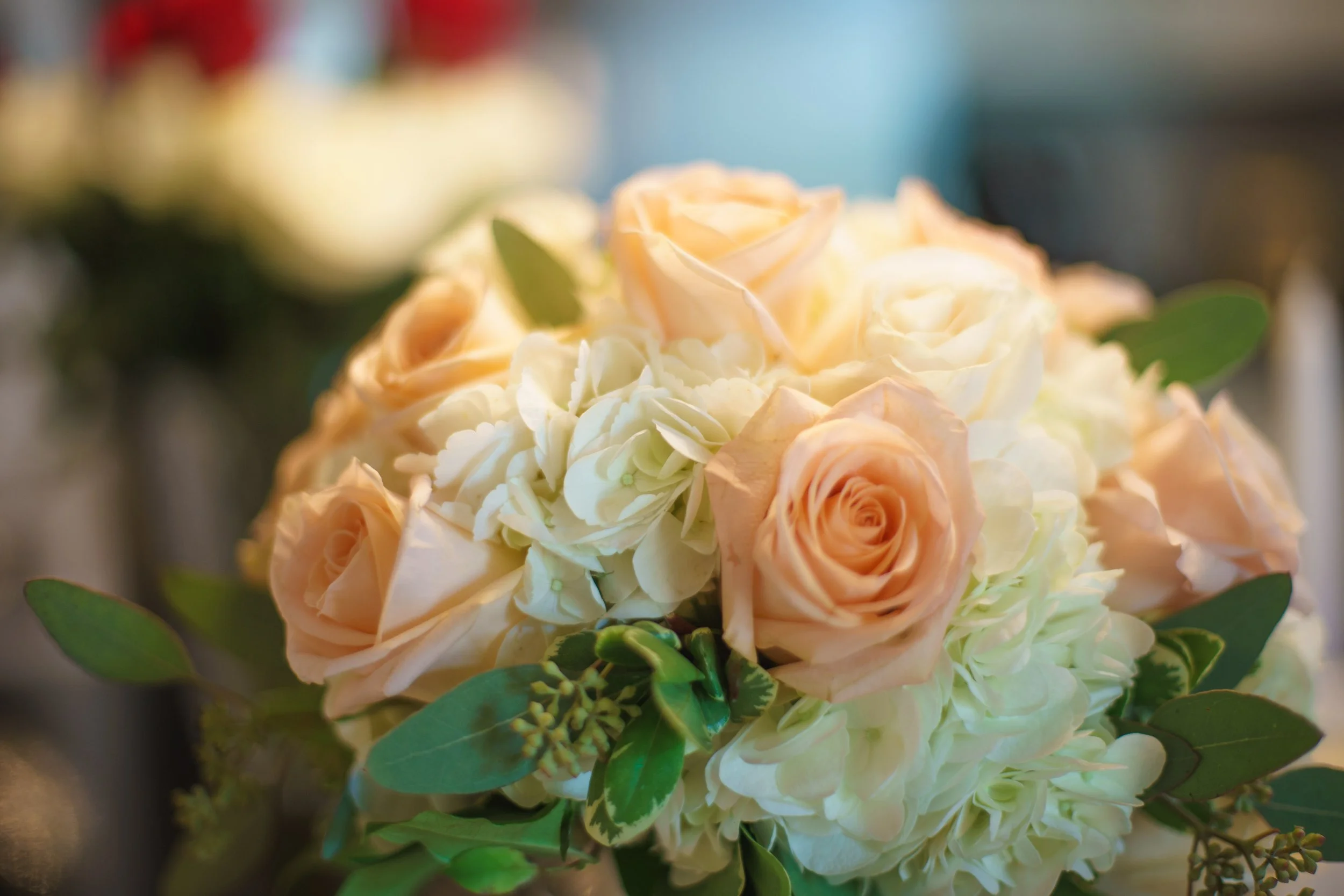 A close-up of a bouquet of peach, white, and cream roses with green leaves.