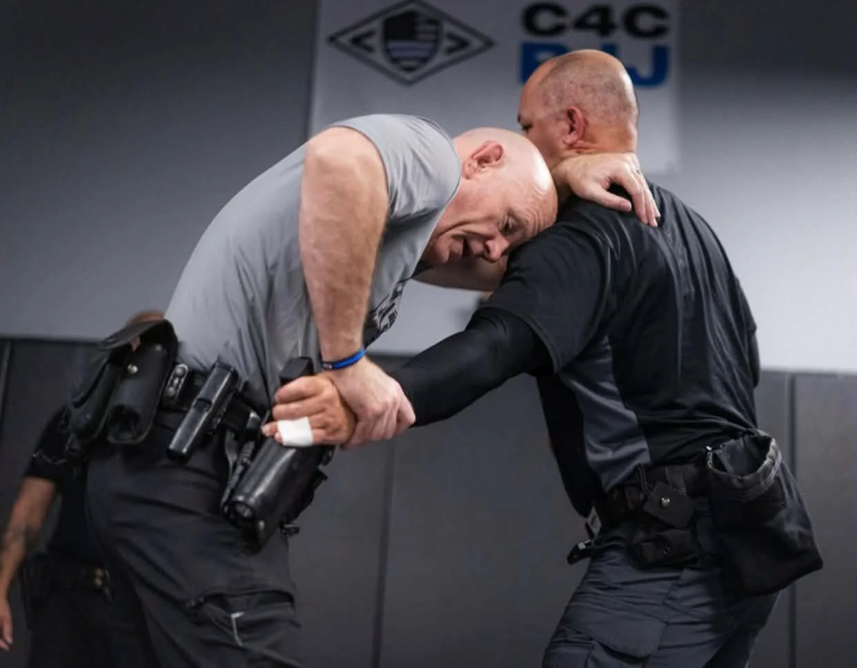 BJJ instructor demonstrating use-of-force defensive tactics to law enforcement officers in a martial arts gym