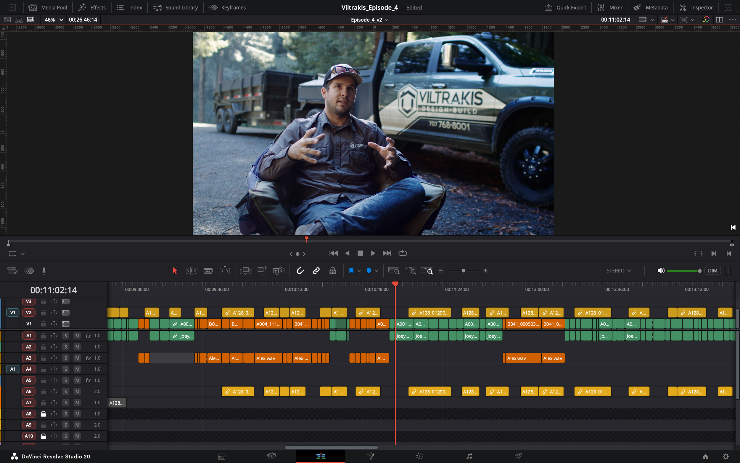 A man sits outdoors next to a pickup truck with the logo 'Viltrakis Design Build' on the side, speaking or explaining with hand gestures.