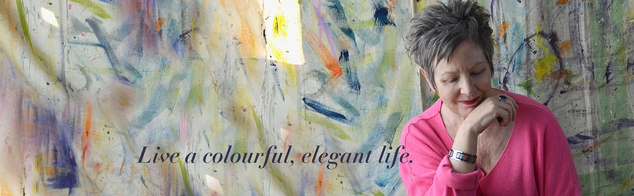 Woman in pink sweater with chin on hand looking downward colourfully painted backdrop