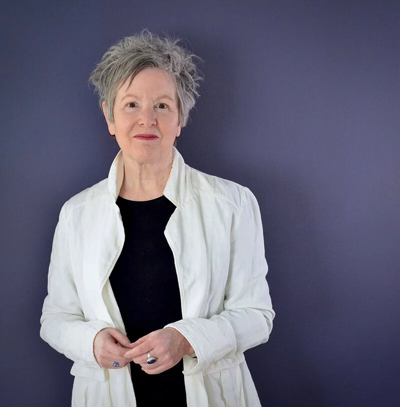 Smiling woman wearing white jacket and black top with dark purple background