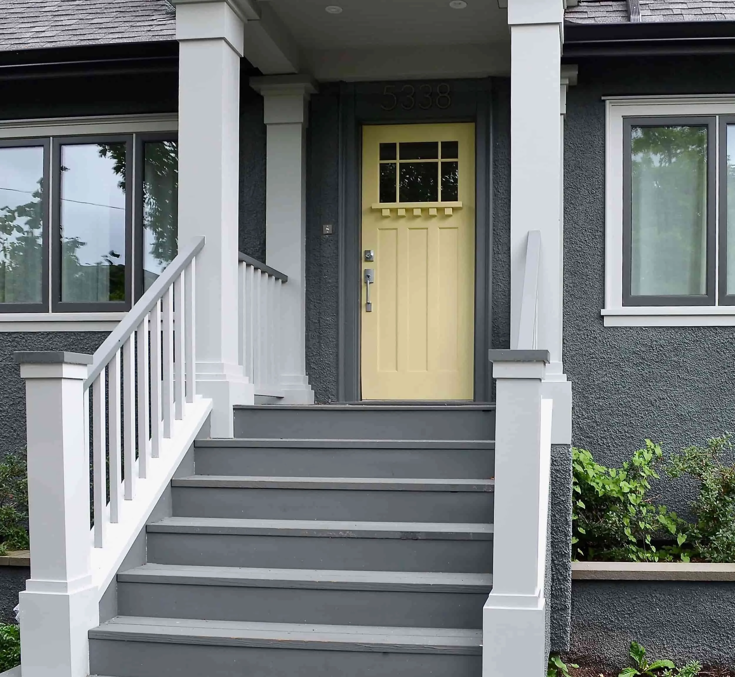 Front porch of house painted in a grey green with yellow door