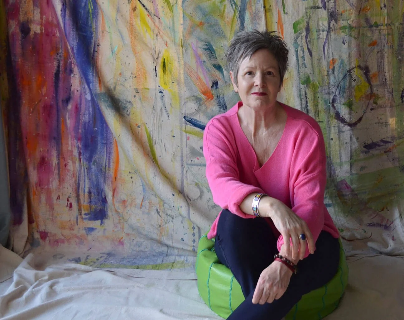 woman sitting on green cushion against a colourfully painted backdrop