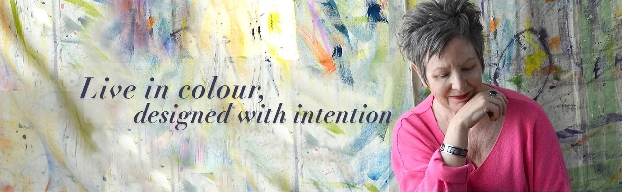 Woman wearing pink sweater with chin on back of hand, colorful painted background