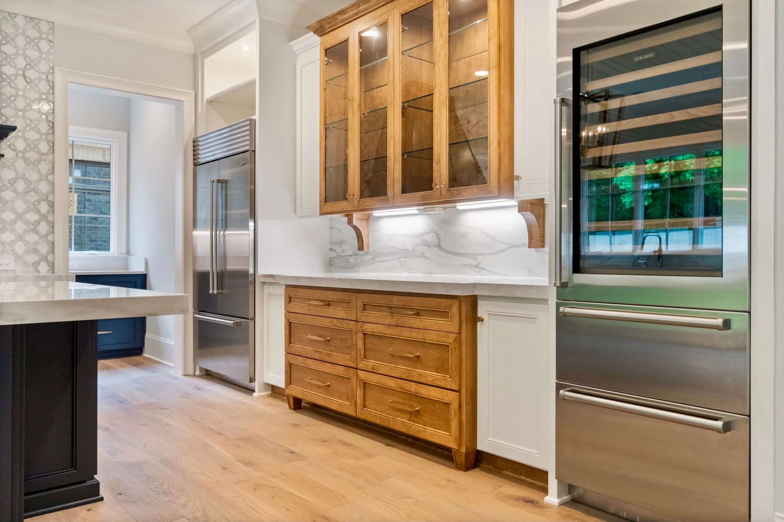 Modern kitchen with light wood and white cabinets, stainless steel appliances, and marble backsplash.