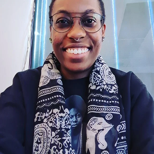 Photo of Michaia Walker in glasses, black shirt, black and white scarf, smiling