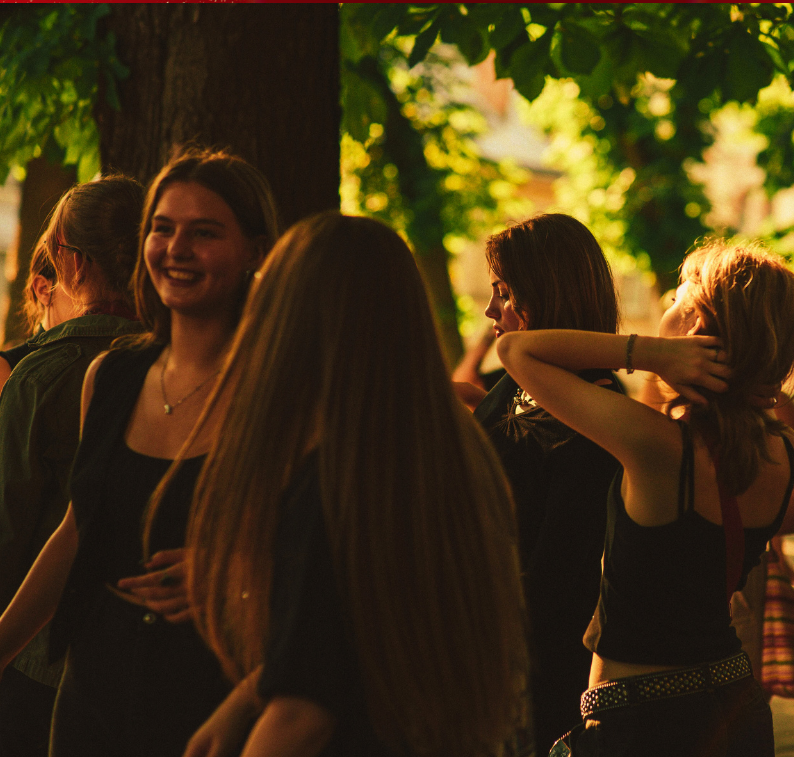 Group of young women standing outdoors in a park with green trees, enjoying a sunny day.
