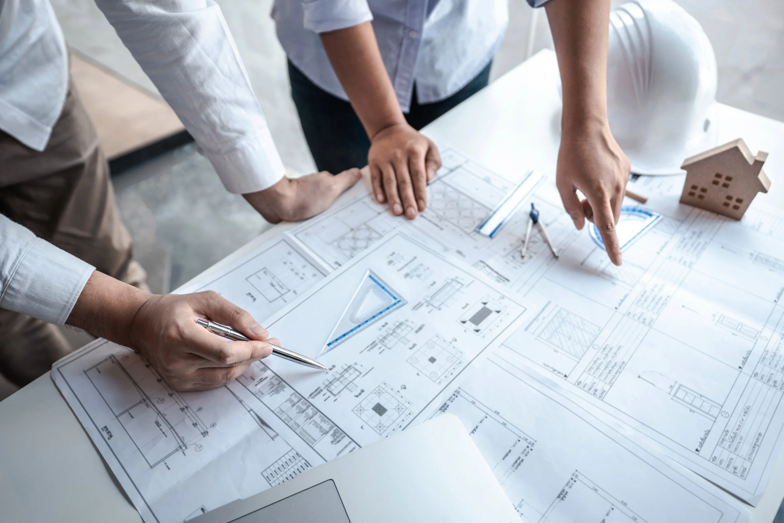 Close-up of two people's hands pointing at a blueprint on a table