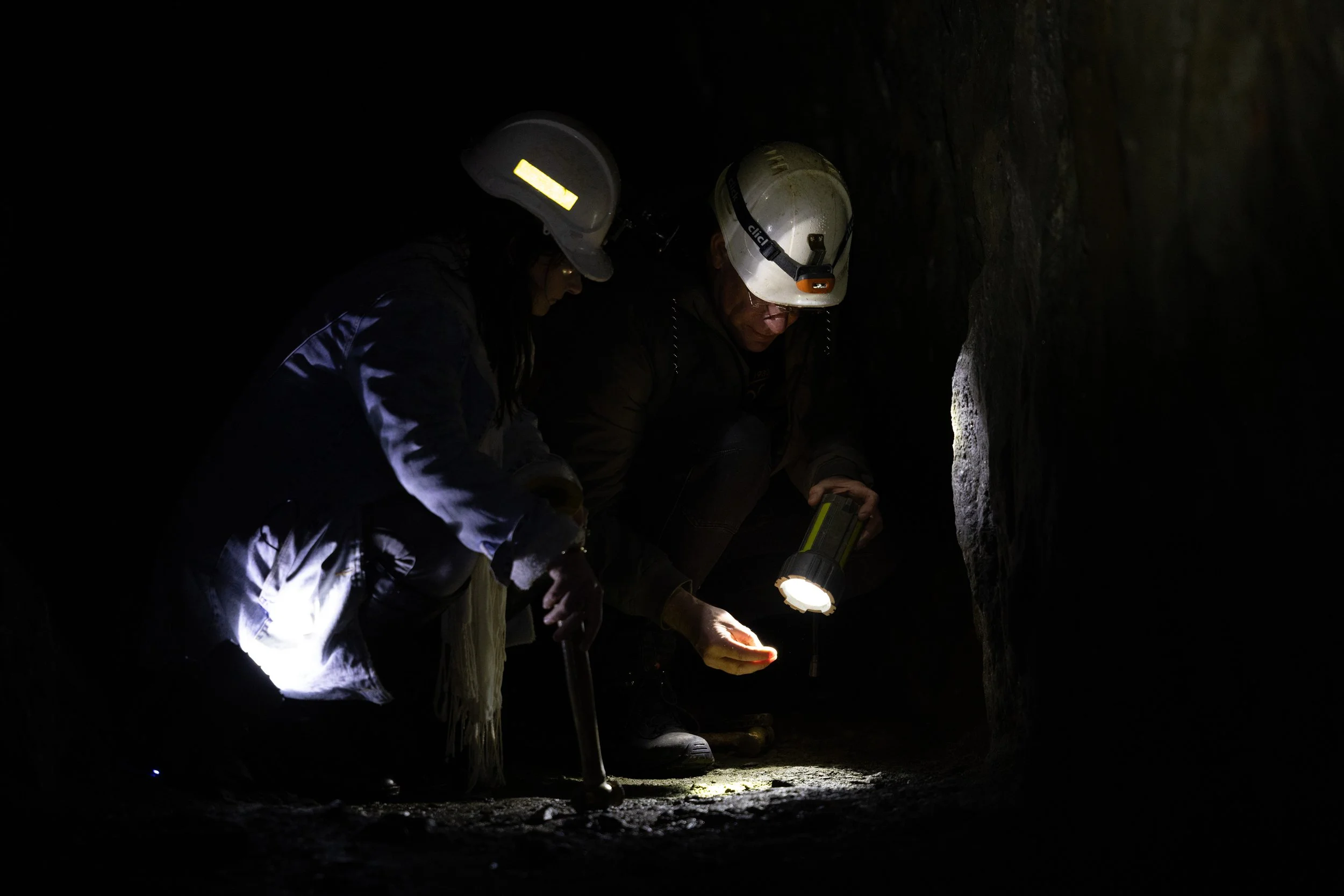 Two people in helmets using a flashlight in a mine shaft