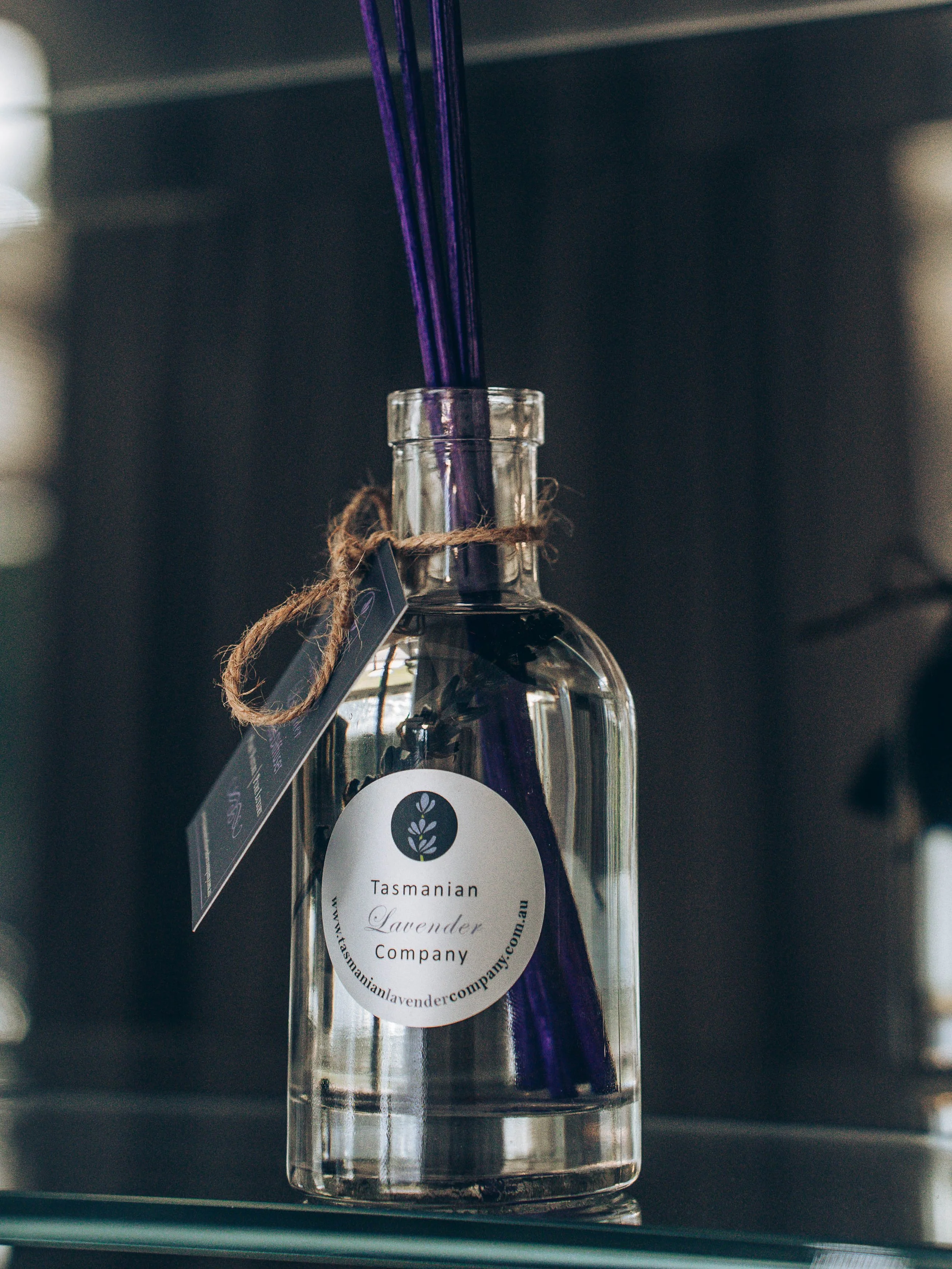 A glass bottle with a label that reads 'Tasmanian Lavender Company' and contains purple lavender sticks.