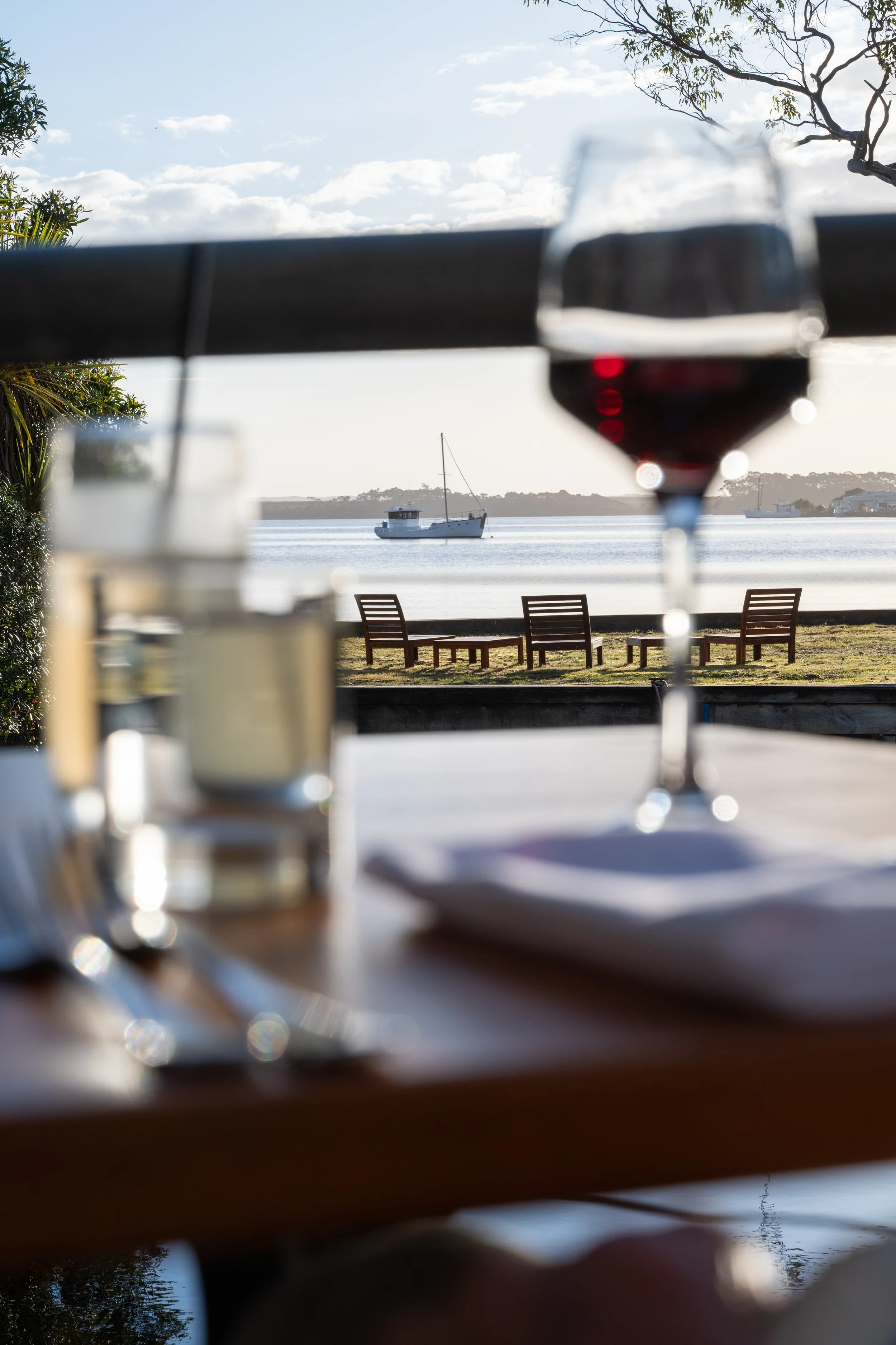A table set for dining with a wine glass and a candle, overlooking the Risby Cove marina with a boat and tree in the background.