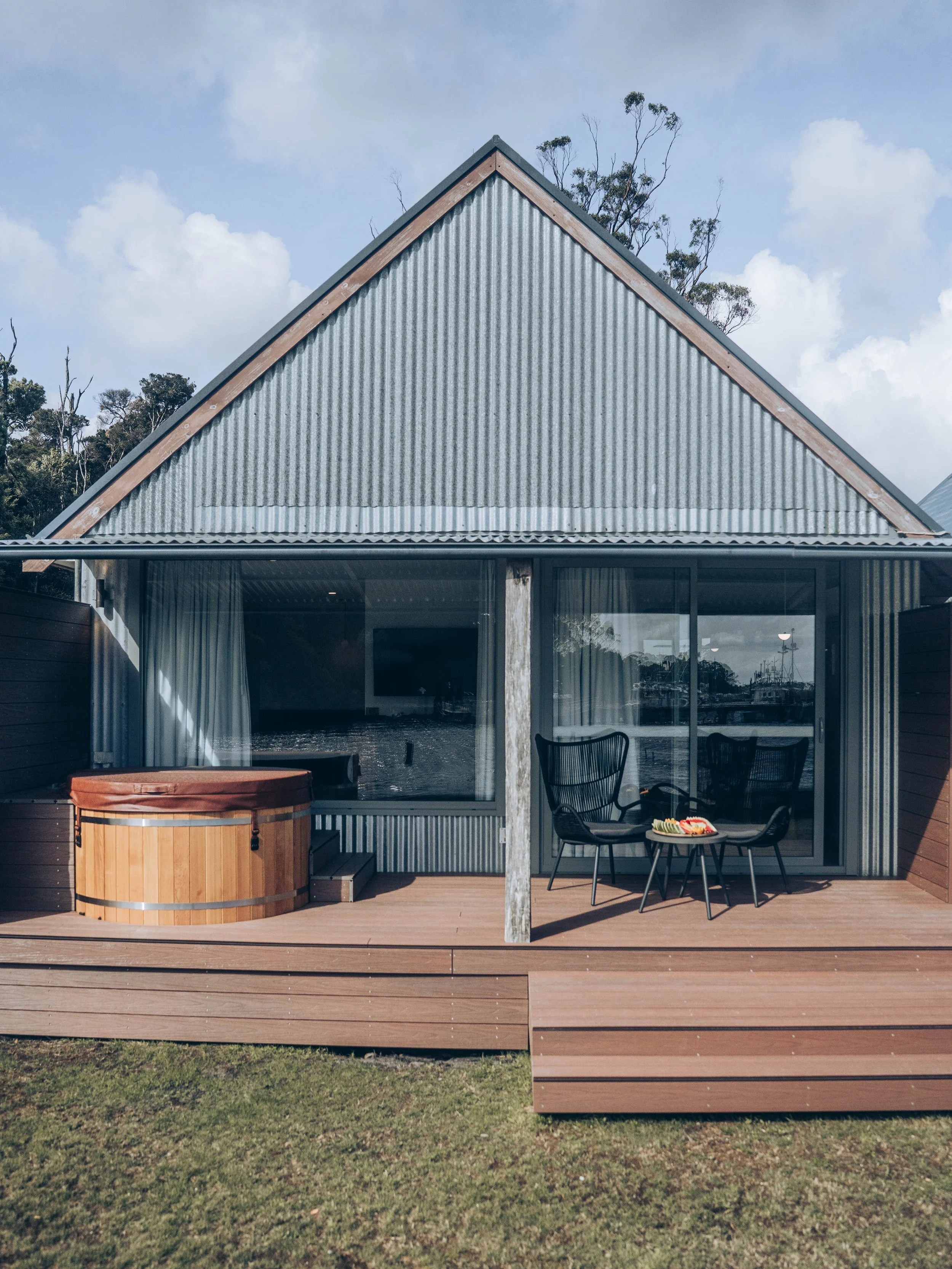 Luxurious pavilion with waterfront covered deck, wooden hot tub, and outdoor chairs.