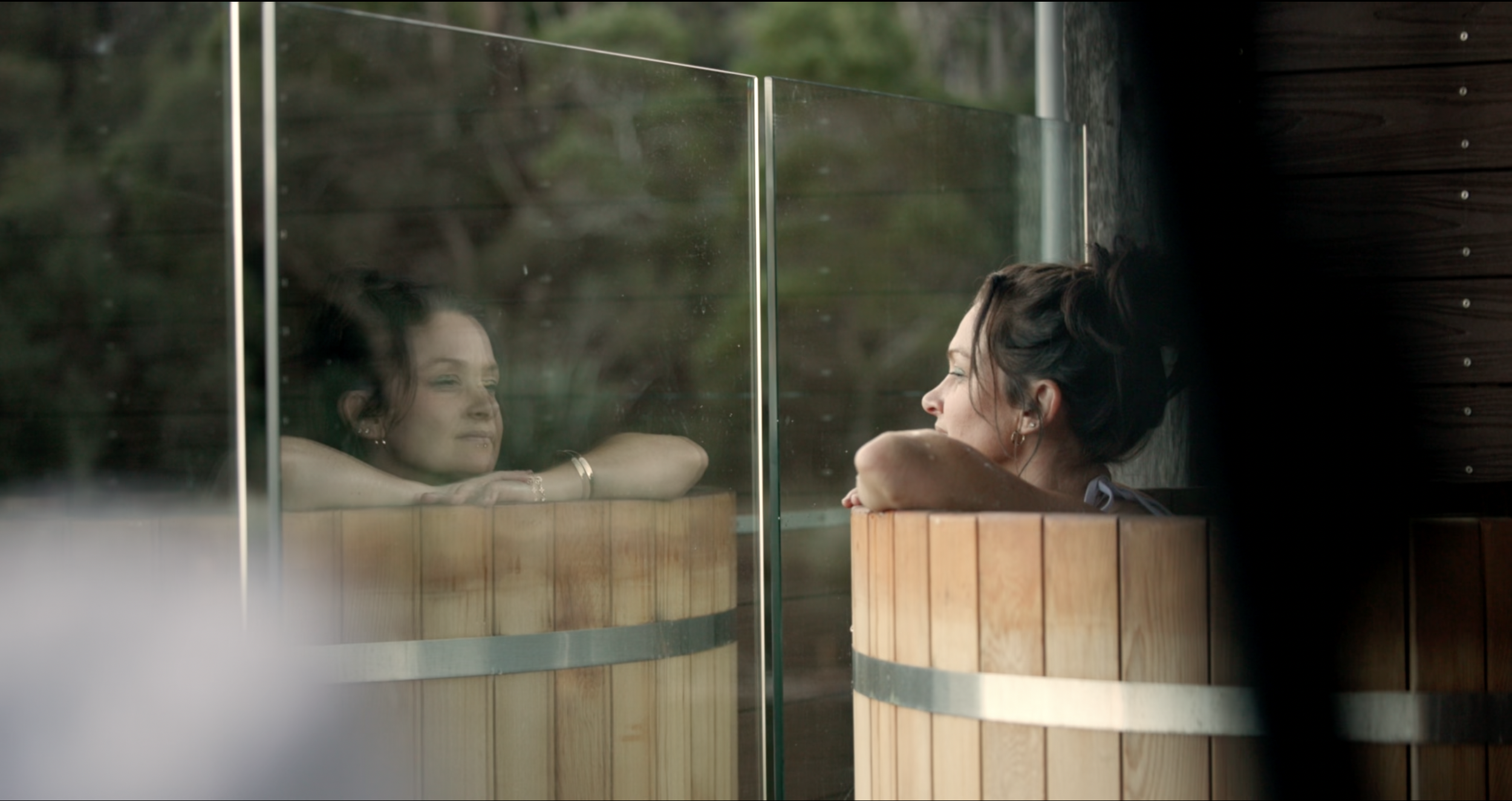A women relaxing in an outdoor cedar hot tub, gazing out towards Macquarie harbour