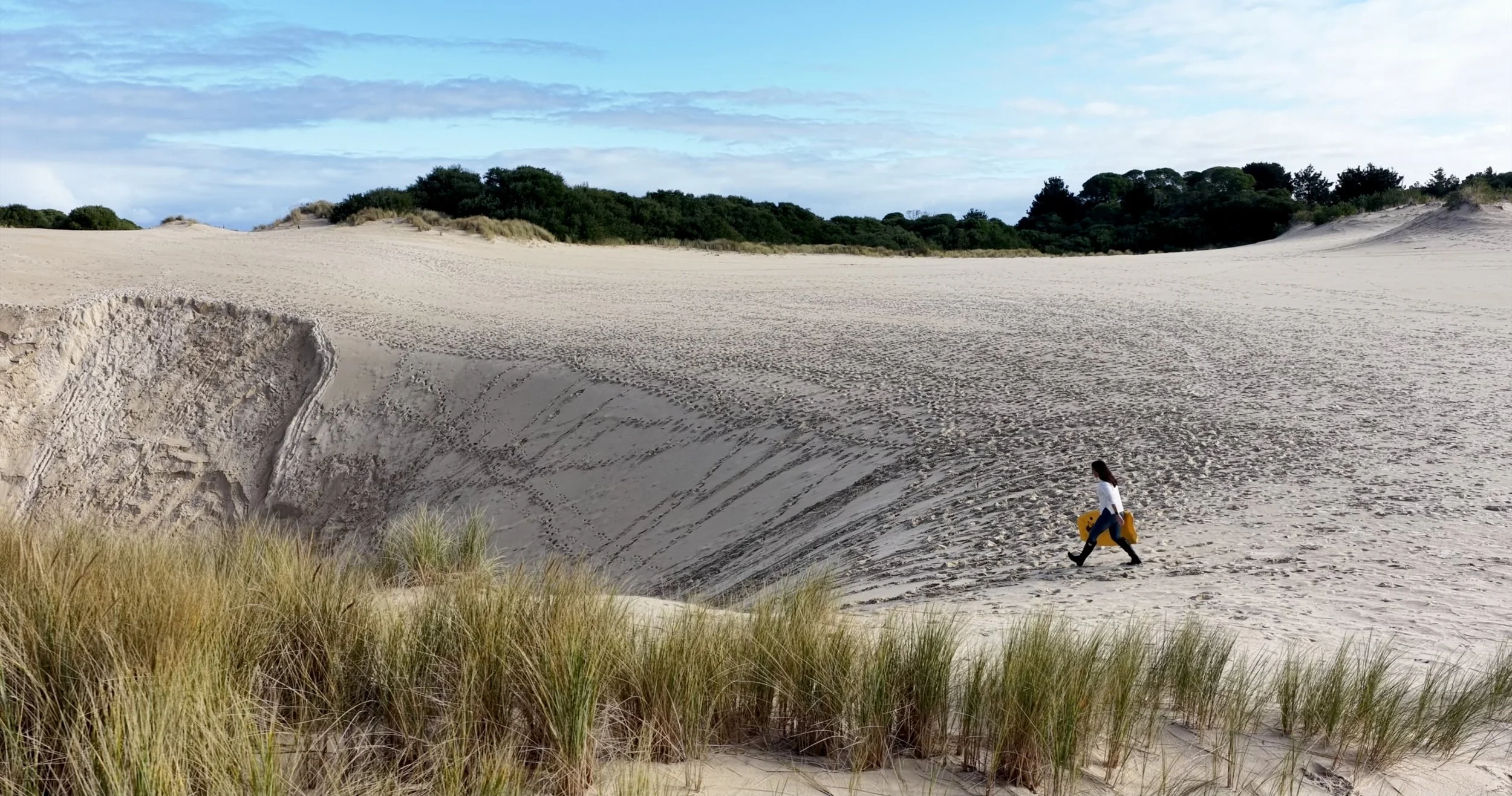 A lady walks to the dune edge at Henty Dunes, preparing to slide down on a boogie board
