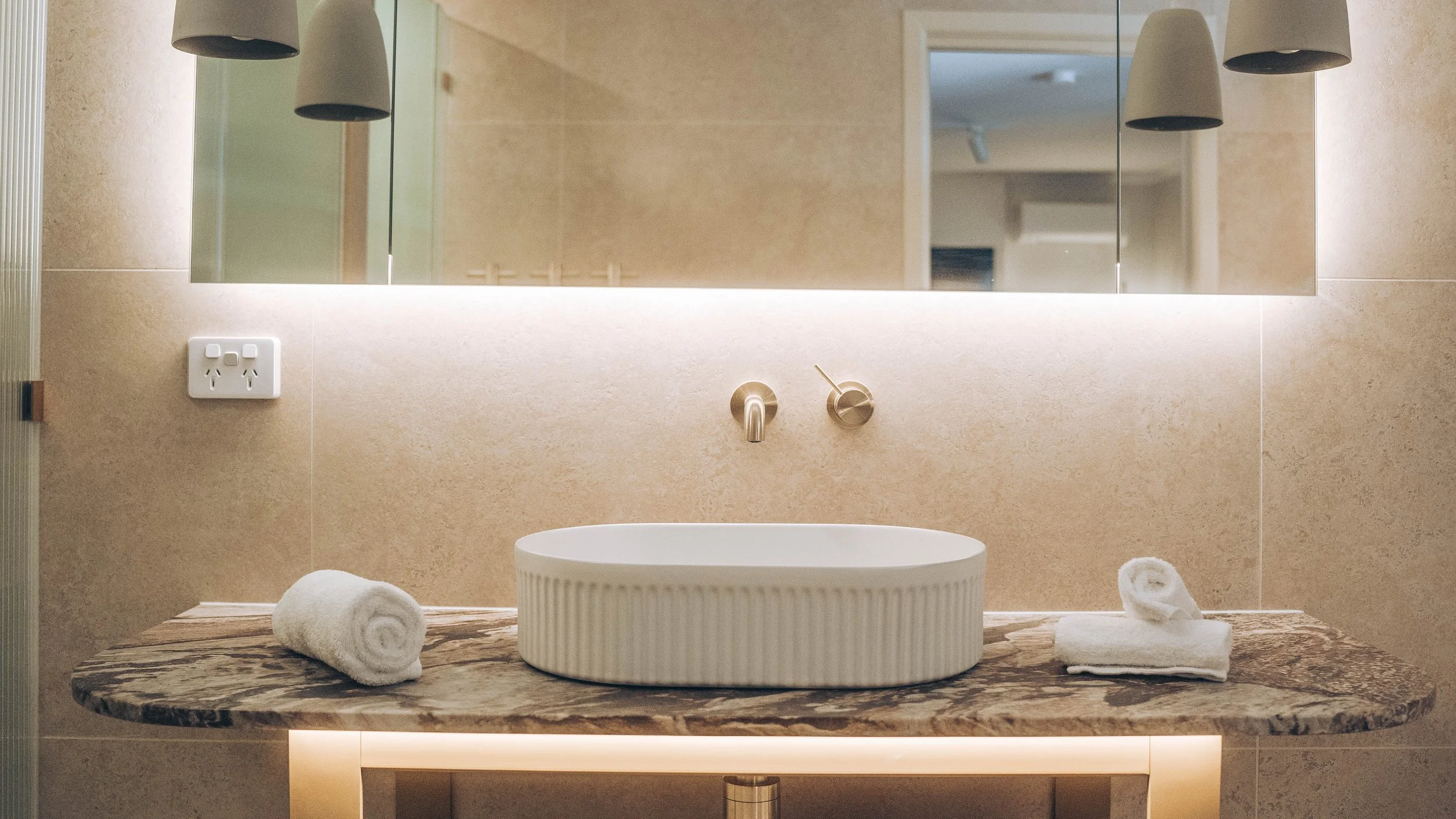 Modern bathroom with a marble countertop, oval sink, wall-mounted faucet, mirror, and pendant lights.
