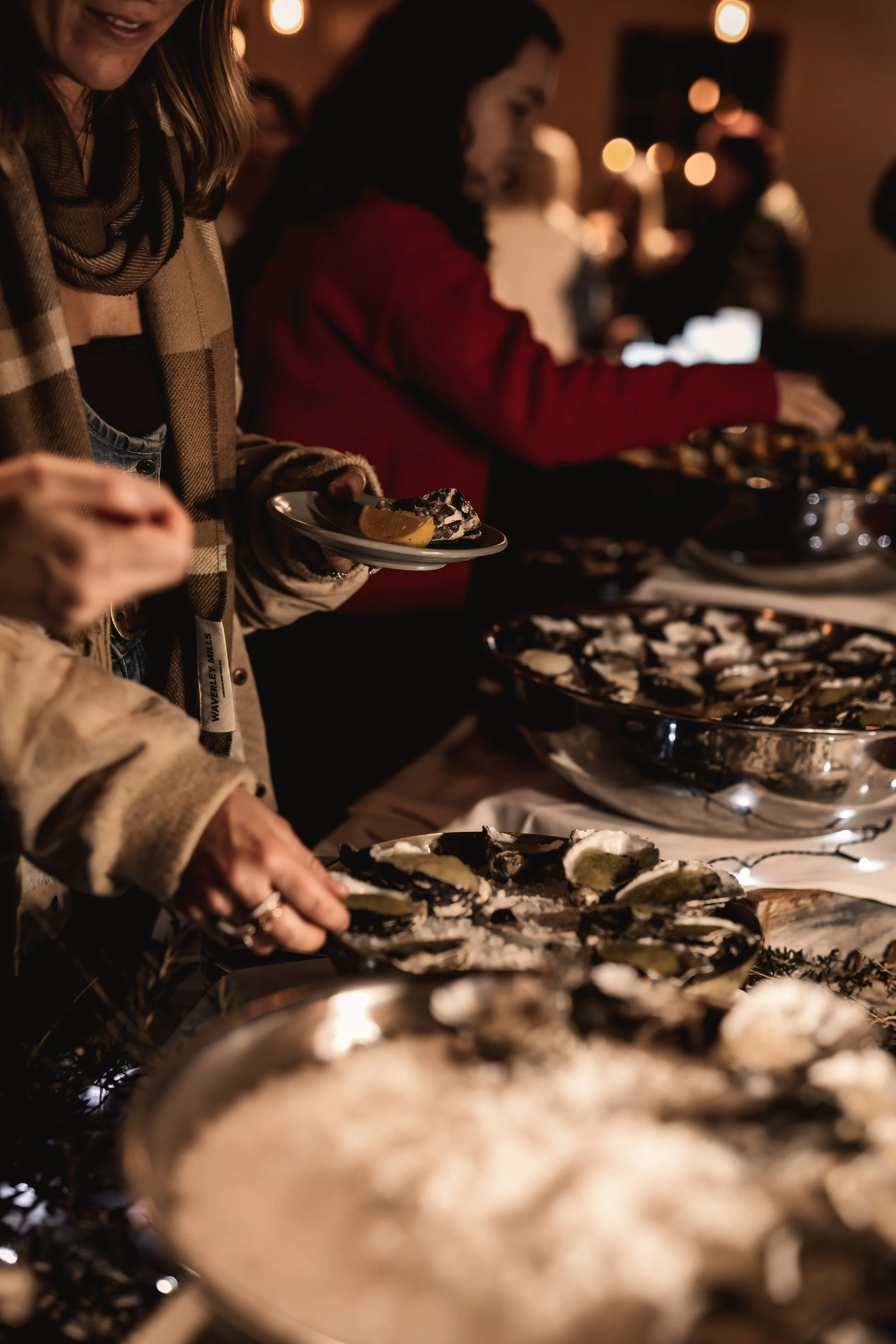 People gathered around serving oysters at a private cocktail party event in The Mill at Risby Cove, with warm ambient lighting in the background.