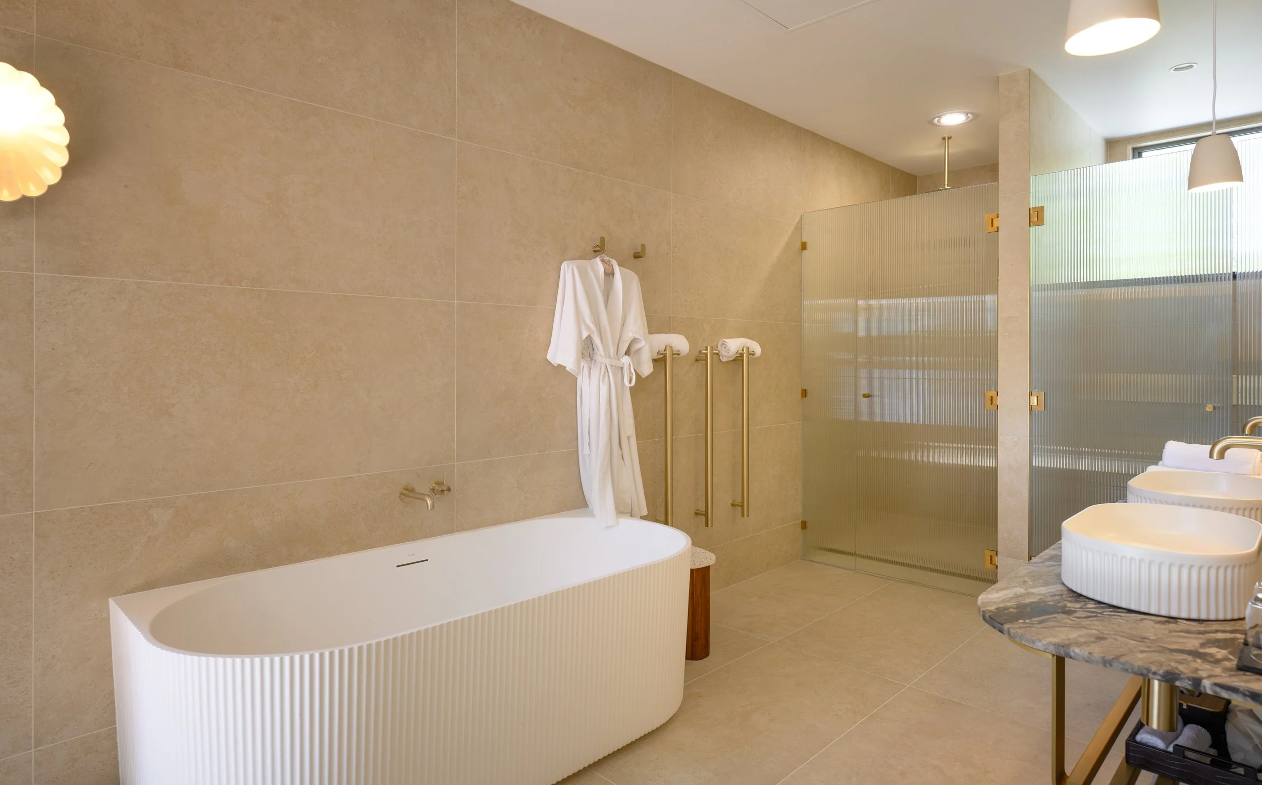 A modern bathroom with a freestanding bathtub, marble countertop sinks, and a frosted glass partition.