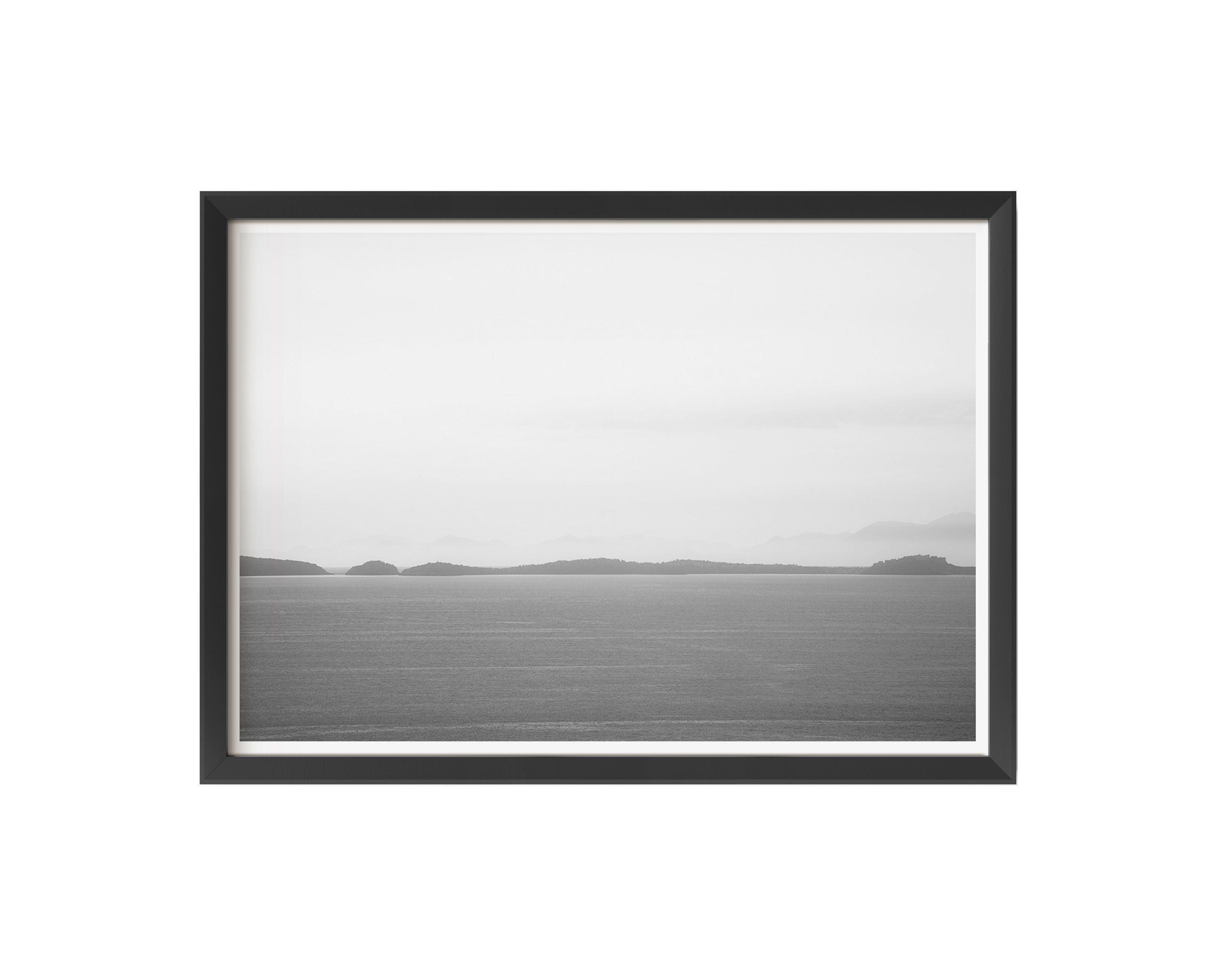 A tranquil black and white fine art photograph capturing a calm sea and misty distant islands beneath a soft, tonal sky.