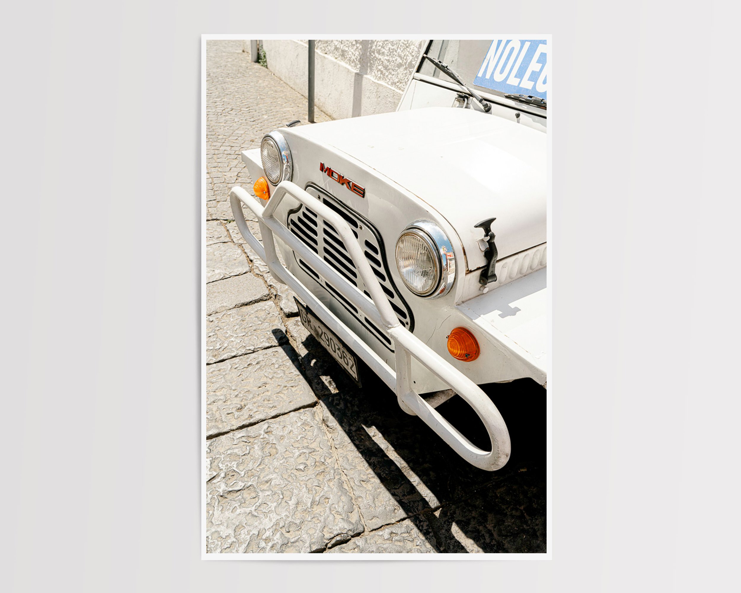 Close-up of vintage white Moke car parked on sunlit cobblestone street in Southern Europe, captured in golden daylight – retro travel photography print by Nicole Toland