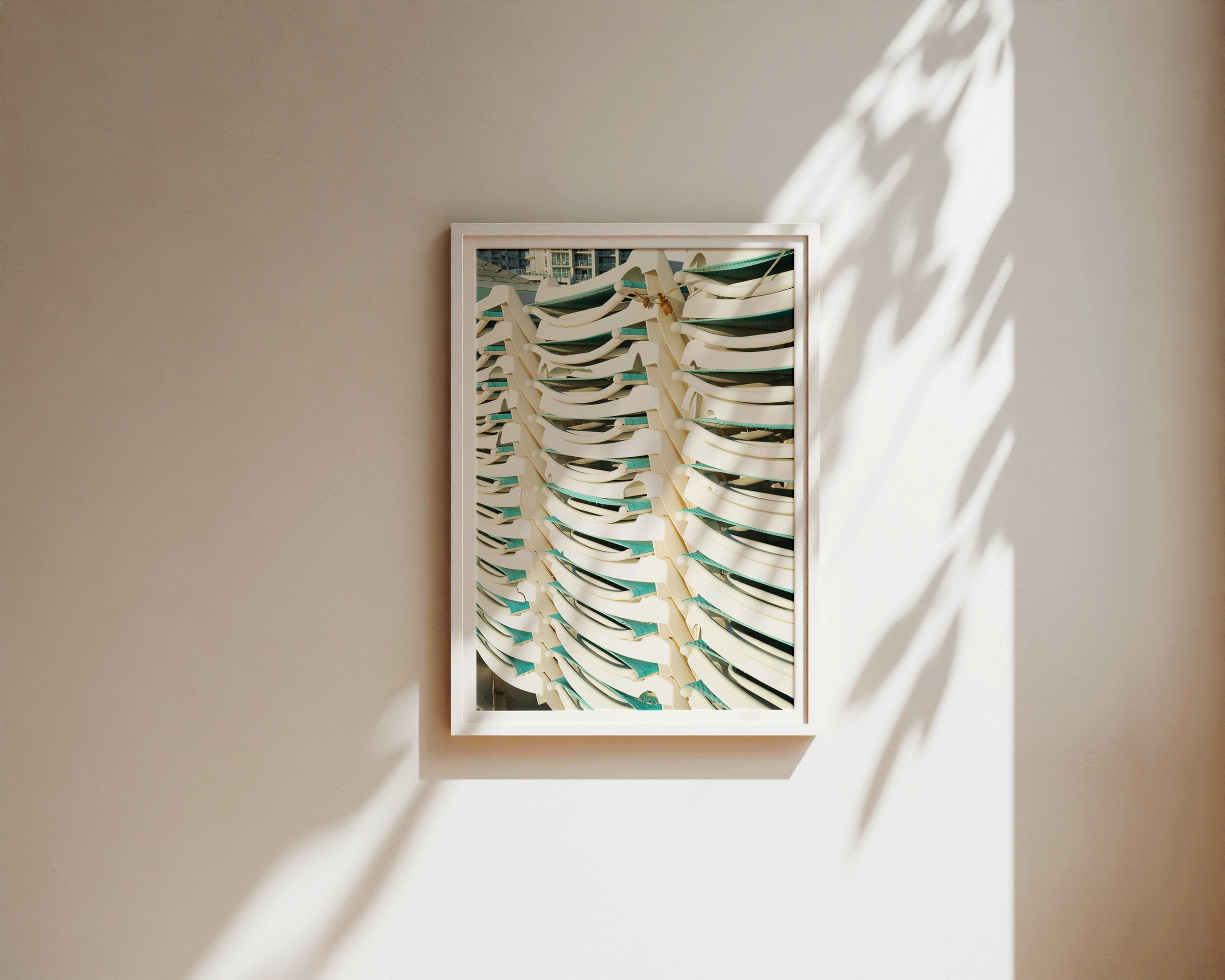 A modern fine art photograph featuring a tightly stacked row of sunlit white and teal lounge chairs, captured with crisp lines and rhythmic repetition.