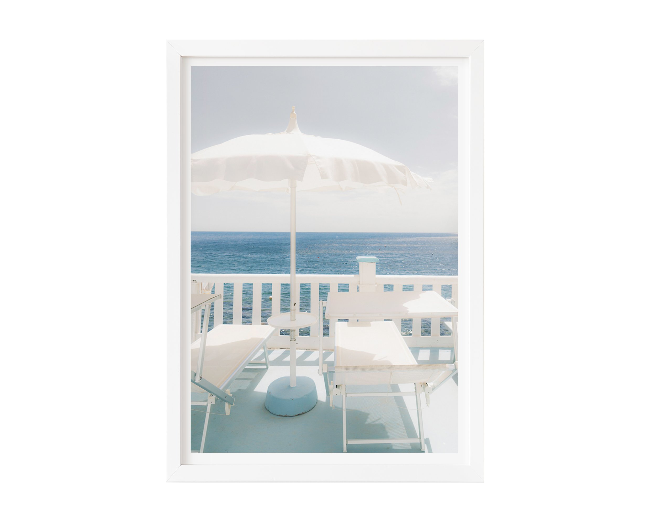 A serene coastal photograph featuring two white lounge chairs and a white umbrella on a pastel-blue balcony overlooking the ocean.