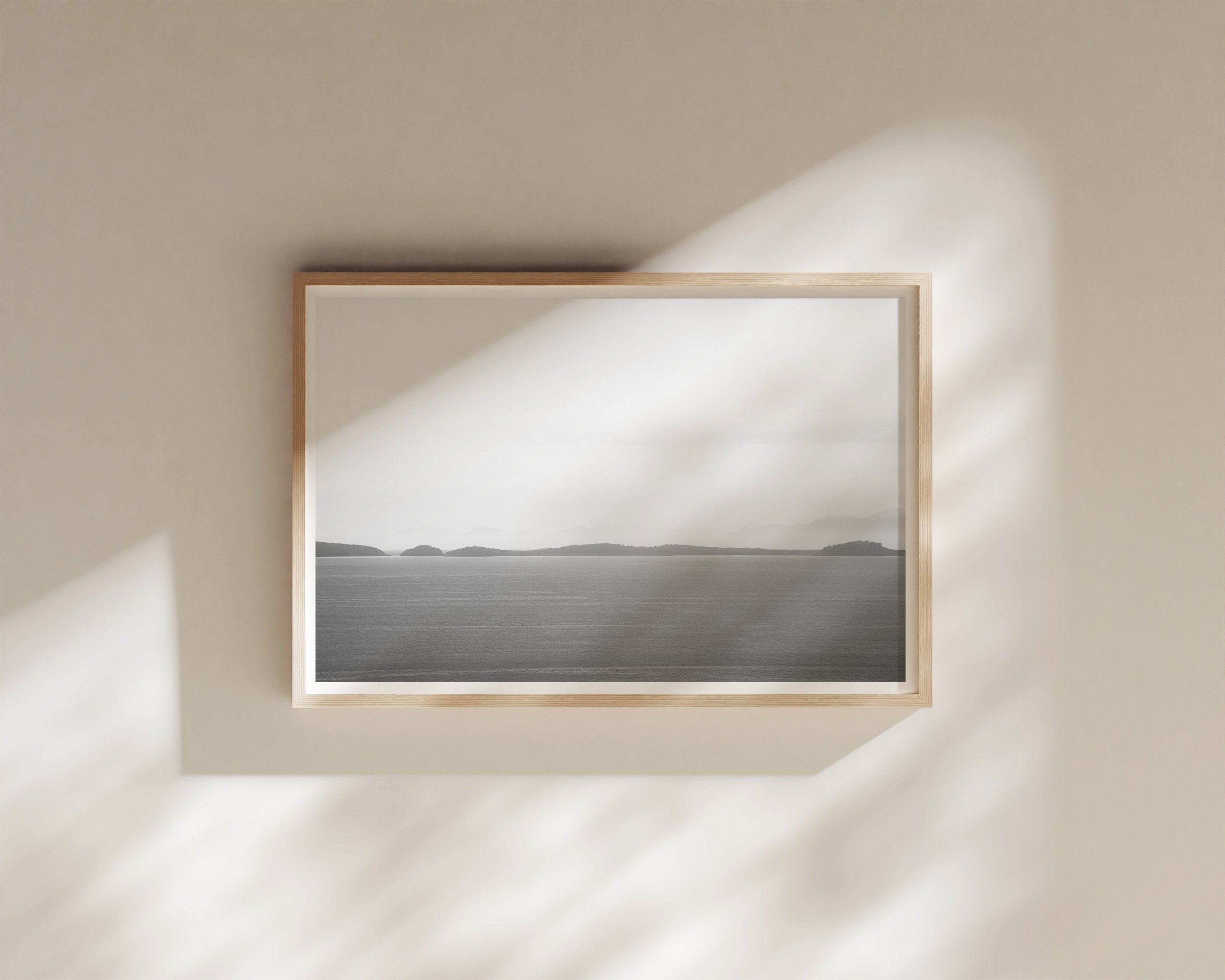 A tranquil black and white fine art photograph capturing a calm sea and misty distant islands beneath a soft, tonal sky.