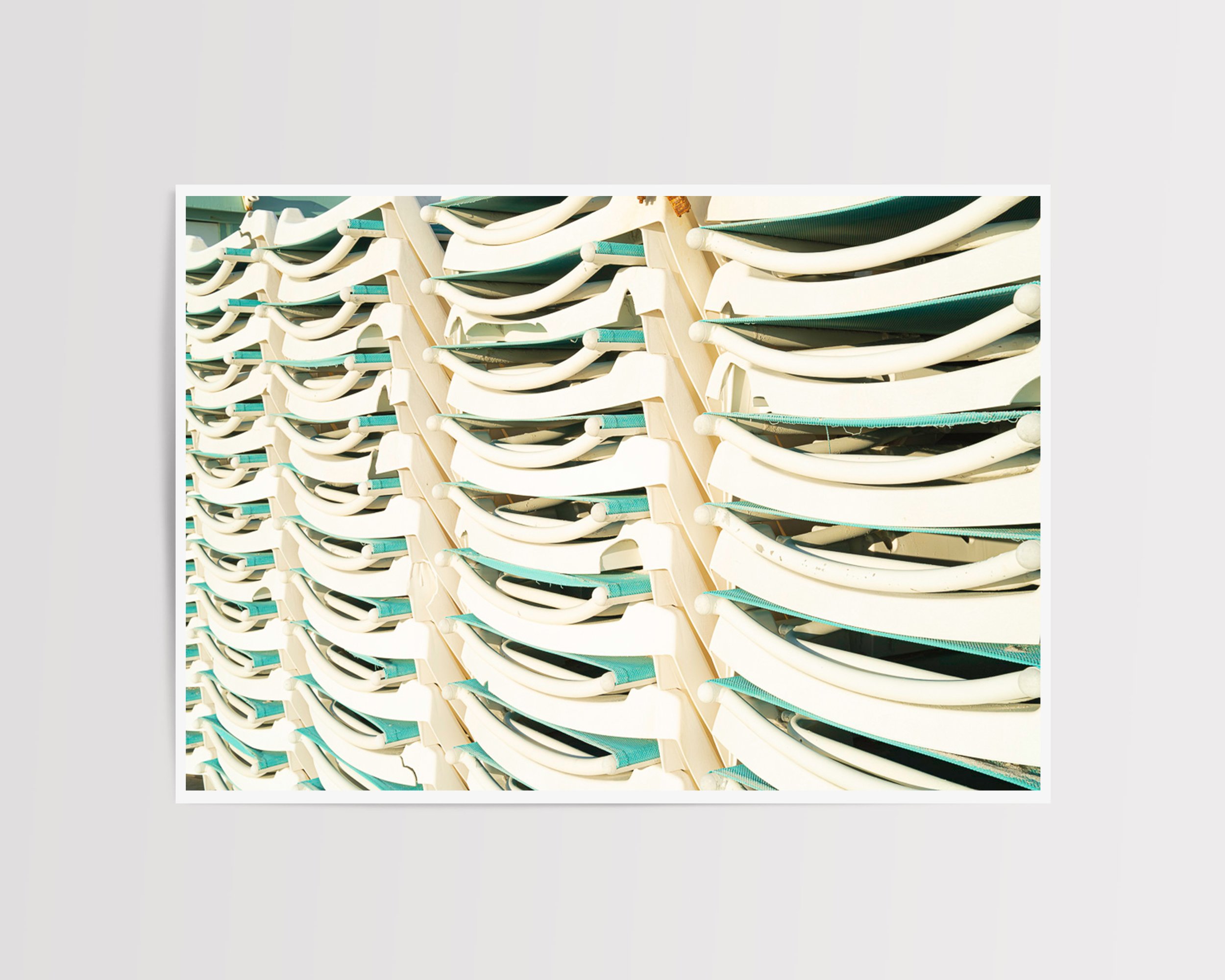 A minimalistic and playful framed fine art print featuring stacked white and teal lounge chairs, bathed in natural sunlight.