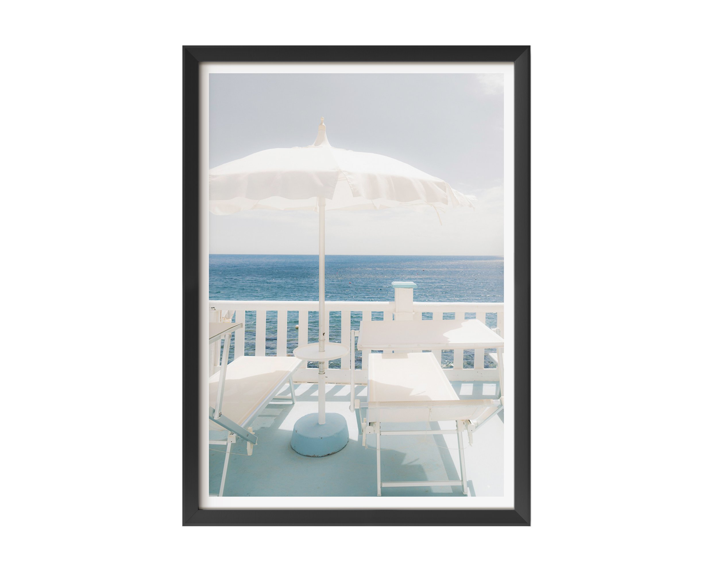 A serene coastal photograph featuring two white lounge chairs and a white umbrella on a pastel-blue balcony overlooking the ocean.