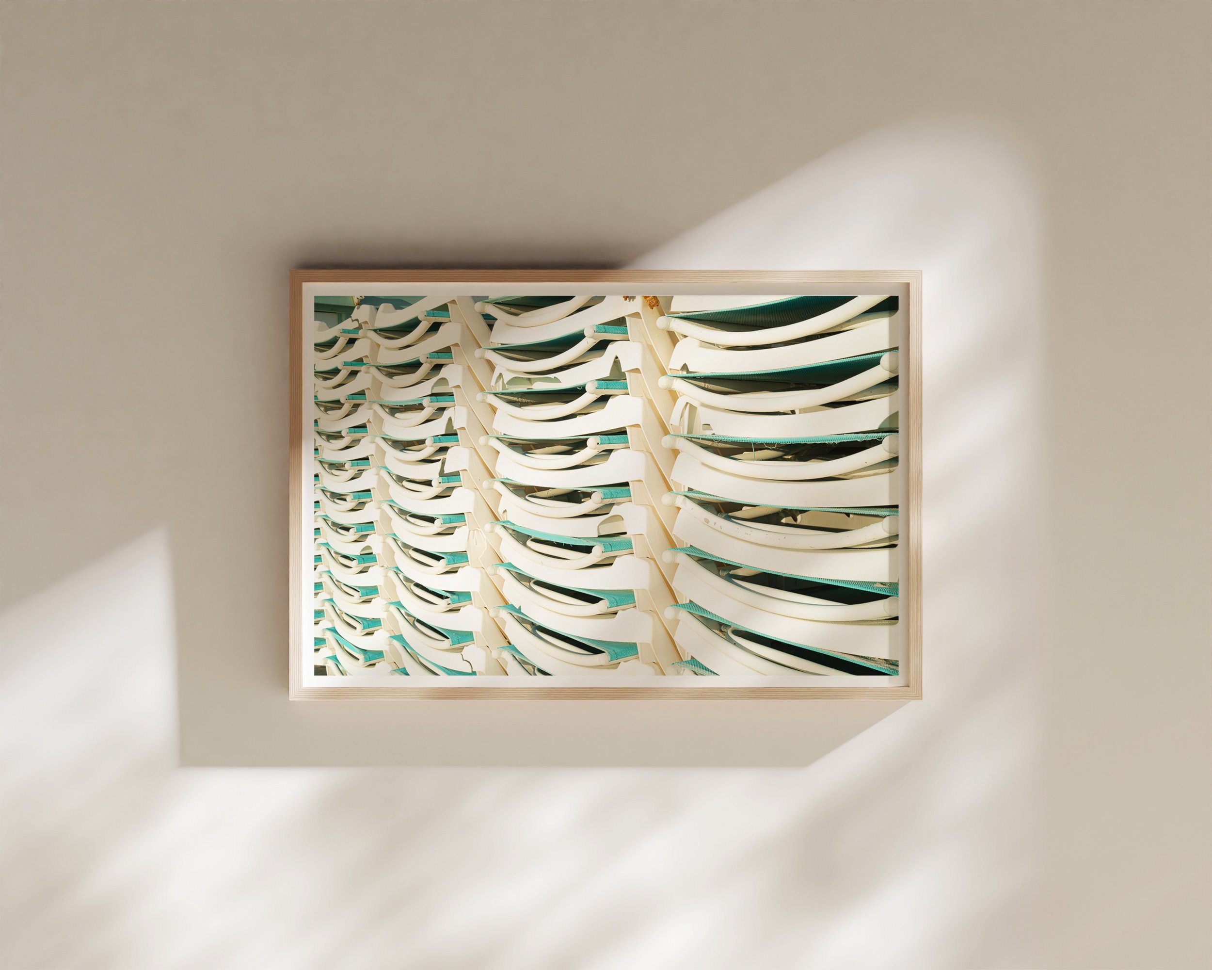 A minimalistic and playful framed fine art print featuring stacked white and teal lounge chairs, bathed in natural sunlight.