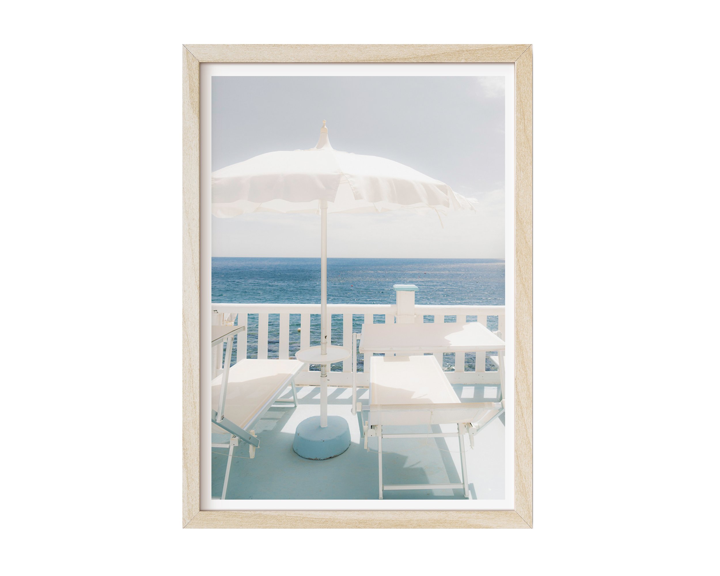 A serene coastal photograph featuring two white lounge chairs and a white umbrella on a pastel-blue balcony overlooking the ocean.