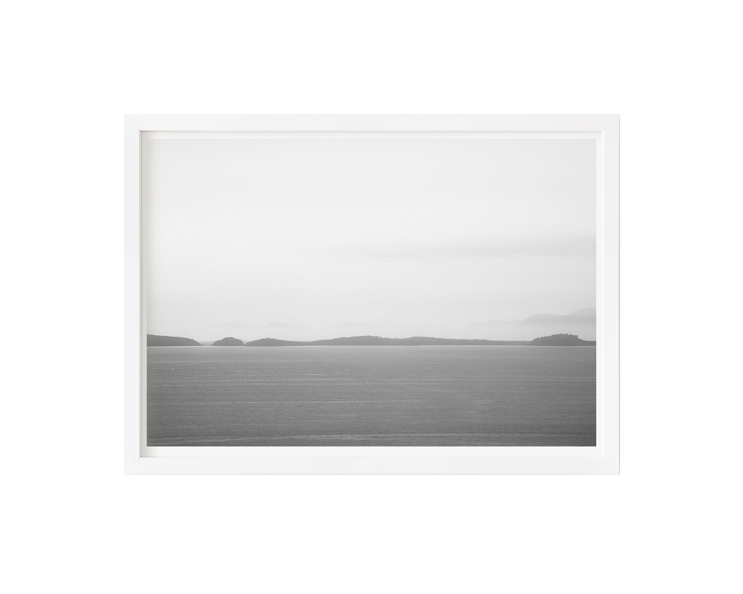 A tranquil black and white fine art photograph capturing a calm sea and misty distant islands beneath a soft, tonal sky.