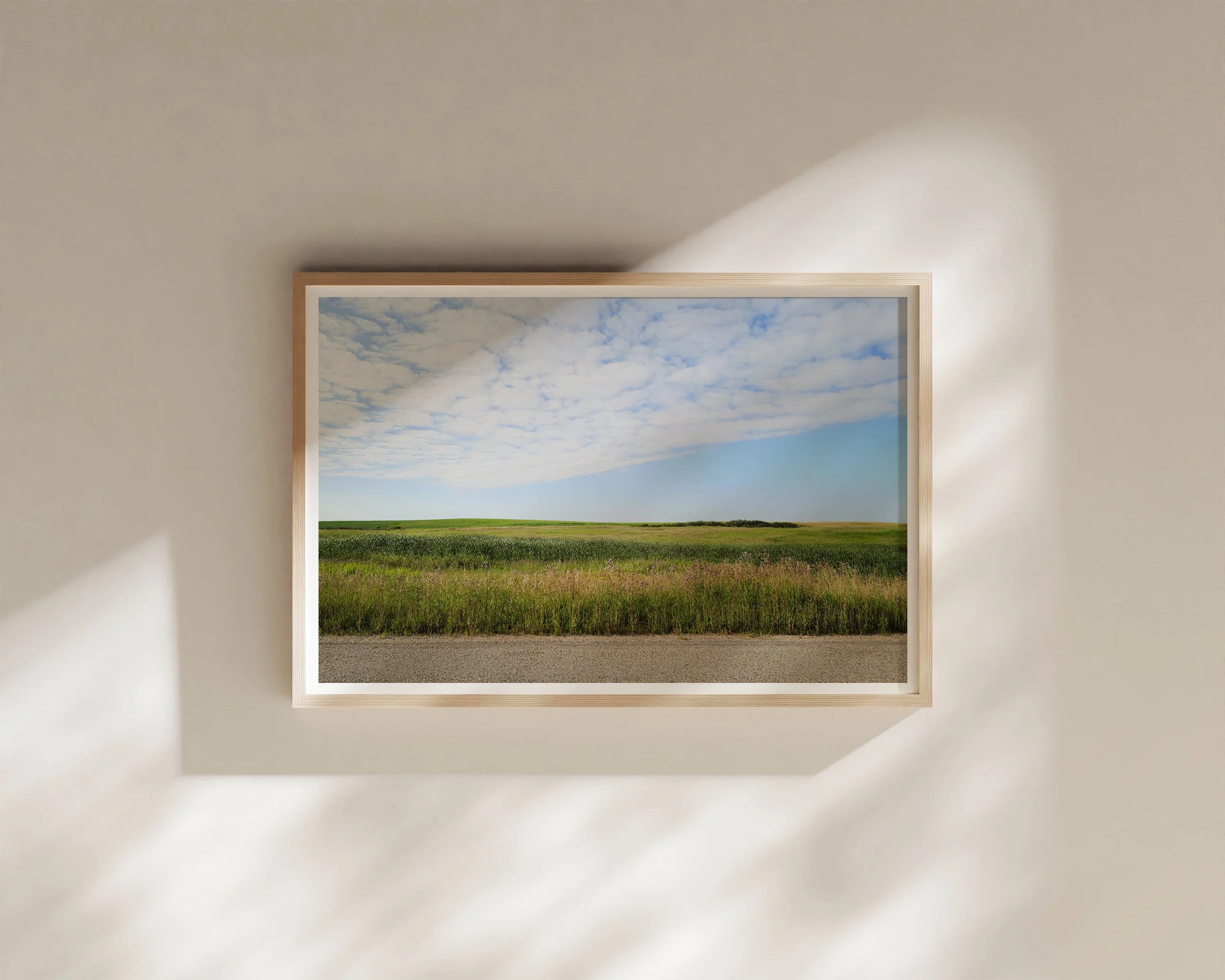 Framed landscape photography print of an open road and grassy fields beneath a soft blue sky, minimalist wall art for modern interiors.