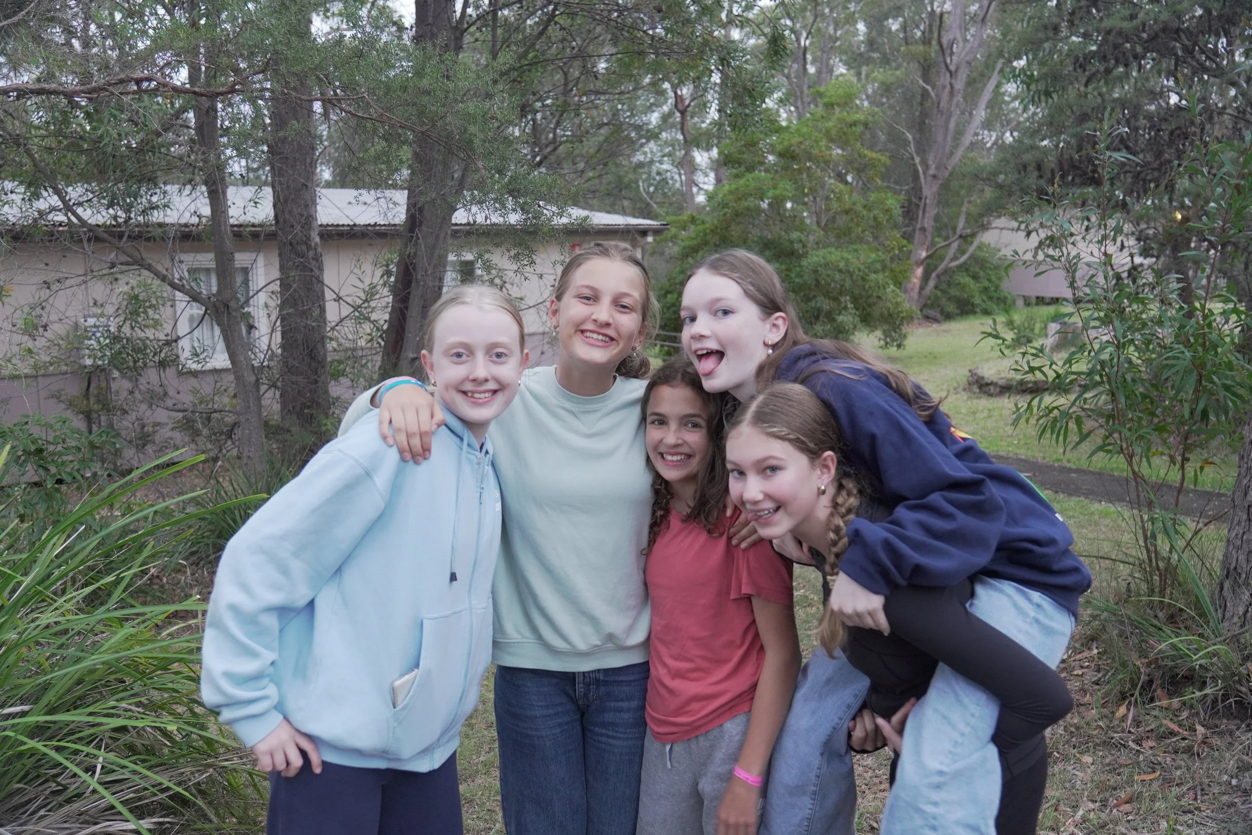 Five girls smiling and posing together outdoors.