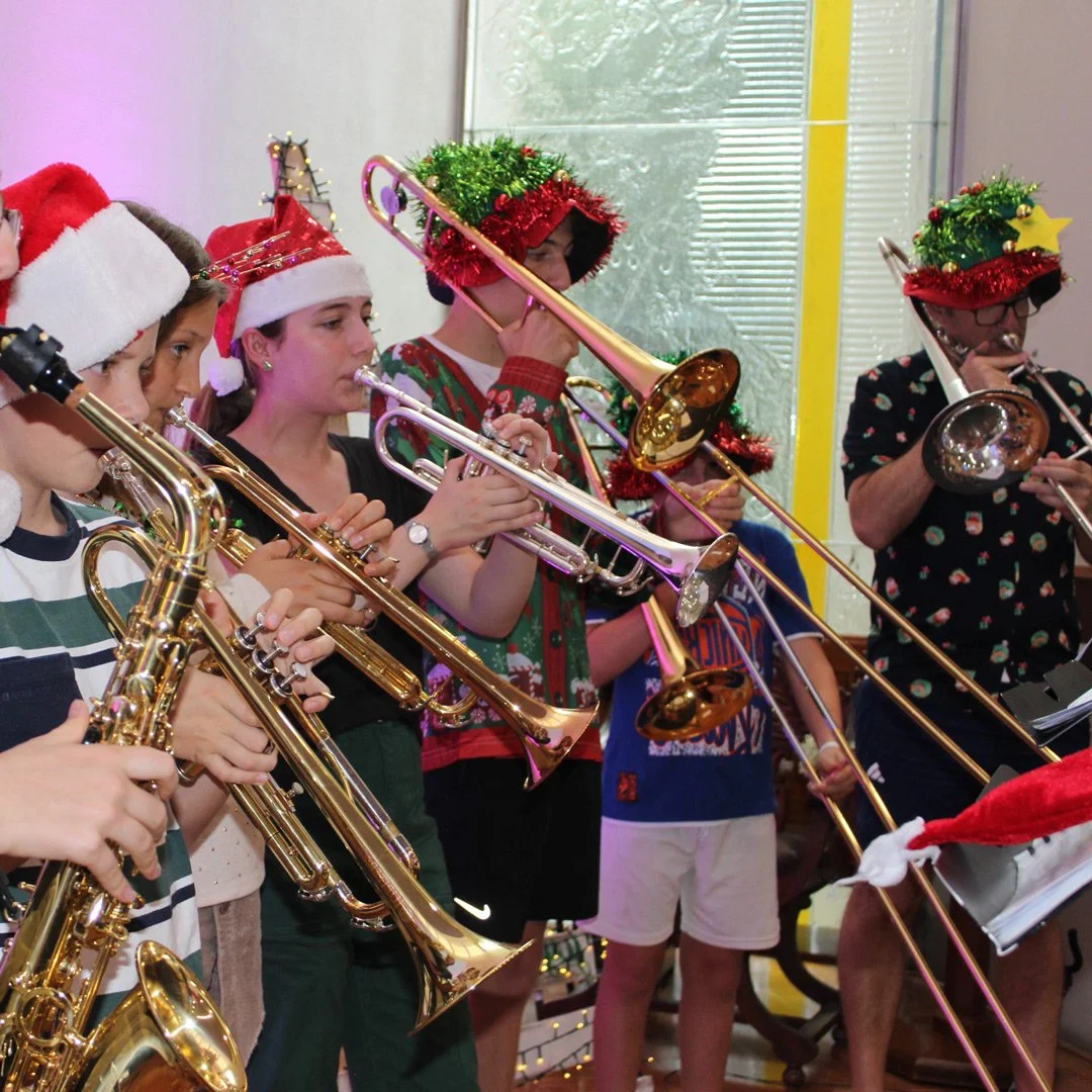 People playing trombones and saxophones, wearing Christmas hats and decorations, during a holiday celebration.