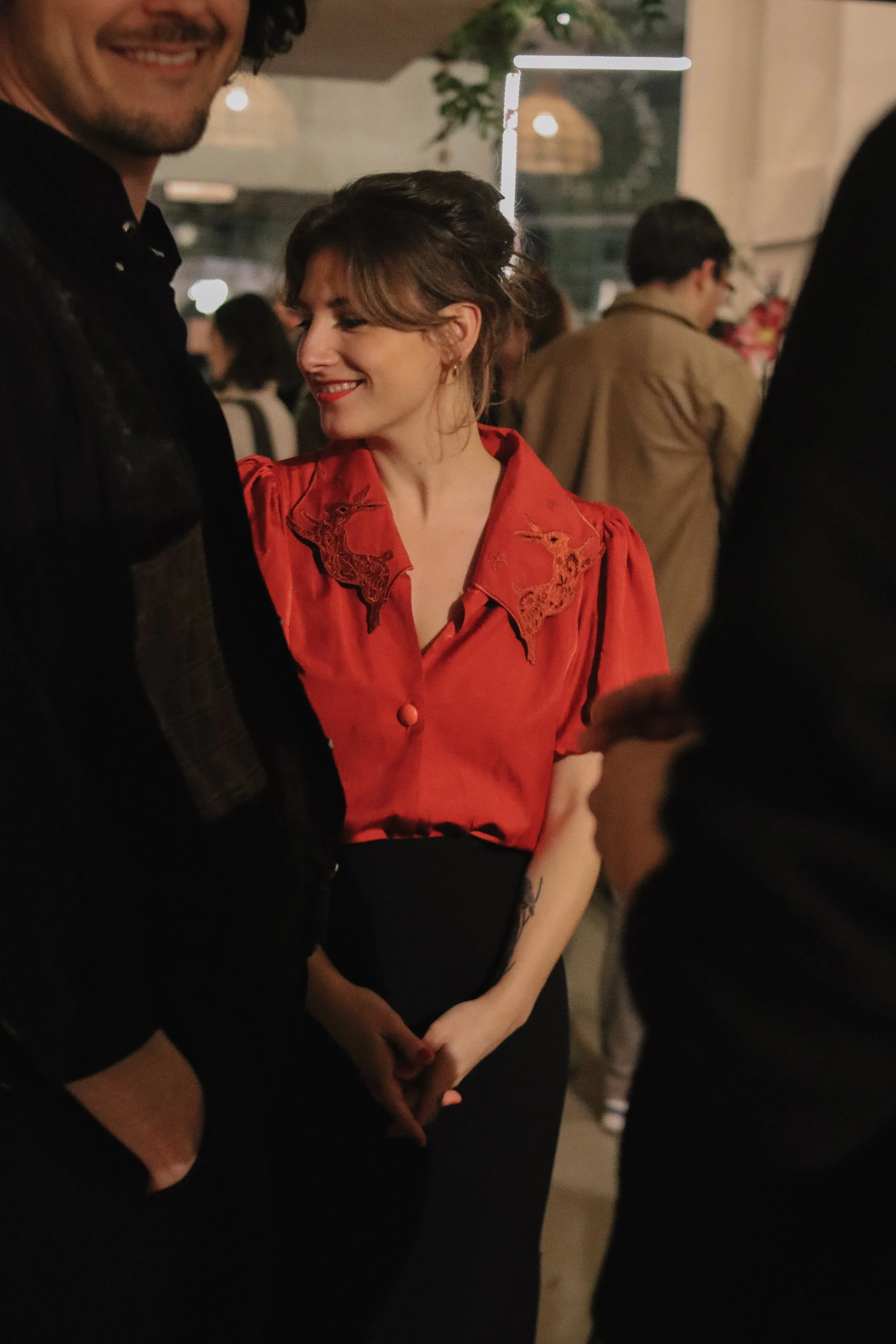 A woman in a red blouse smiling at a man at a social gathering or party.