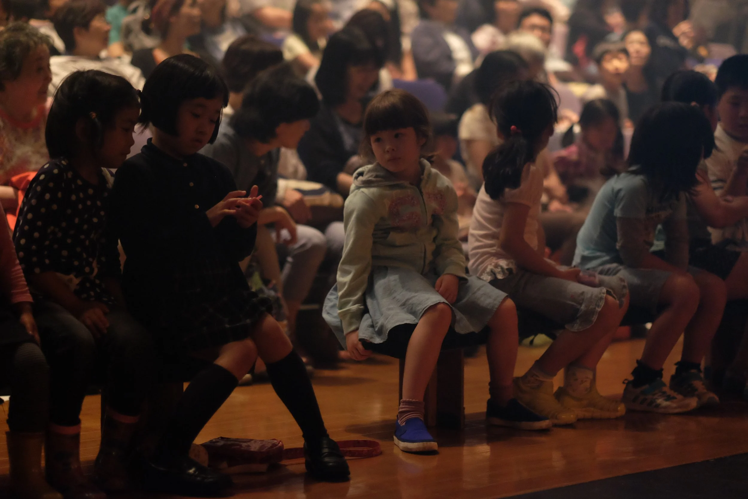 Children sitting on benches in an auditorium or theater during a performance or event.