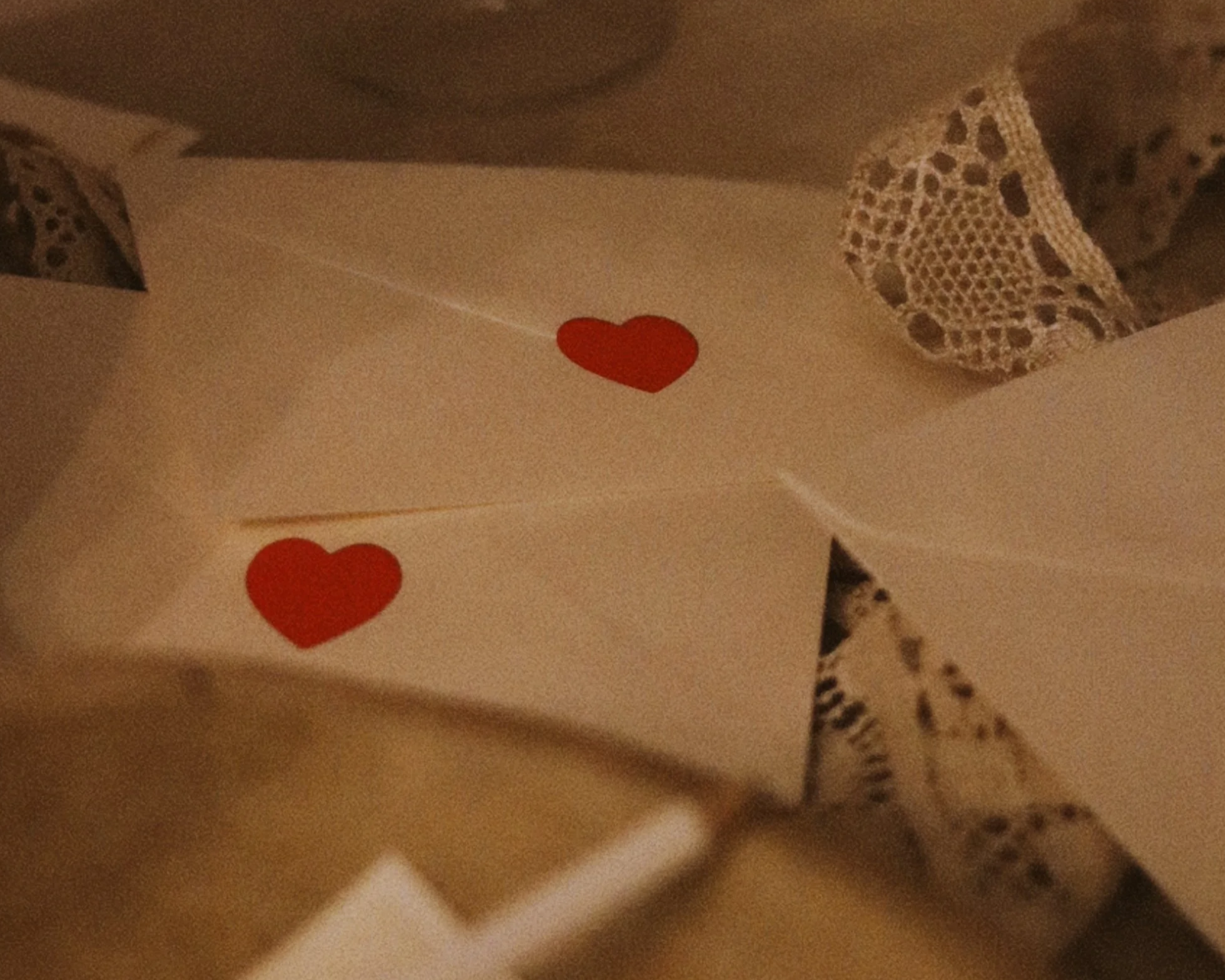 A greeting card with two red heart stickers inside, surrounded by lace and paper with floral patterns.