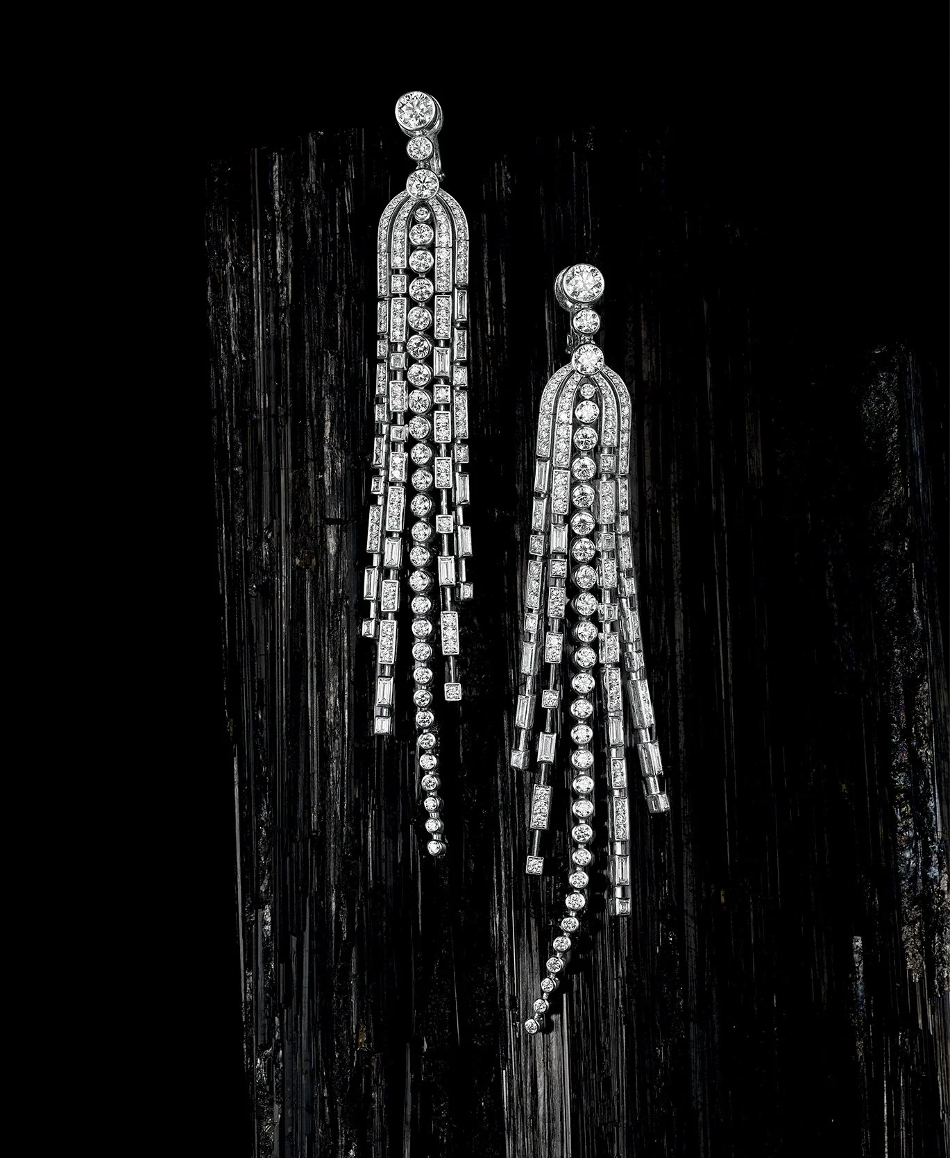 A pair of long, dangling diamond earrings on a dark background.