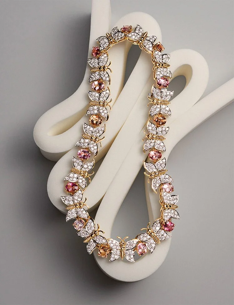A butterfly-shaped diamond and pink gemstone necklace displayed on a white decorative object.