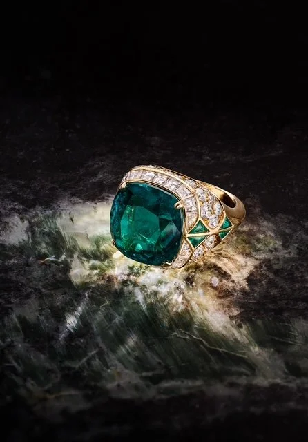 Gold ring with a large green gemstone and small diamonds on a dark, textured surface.