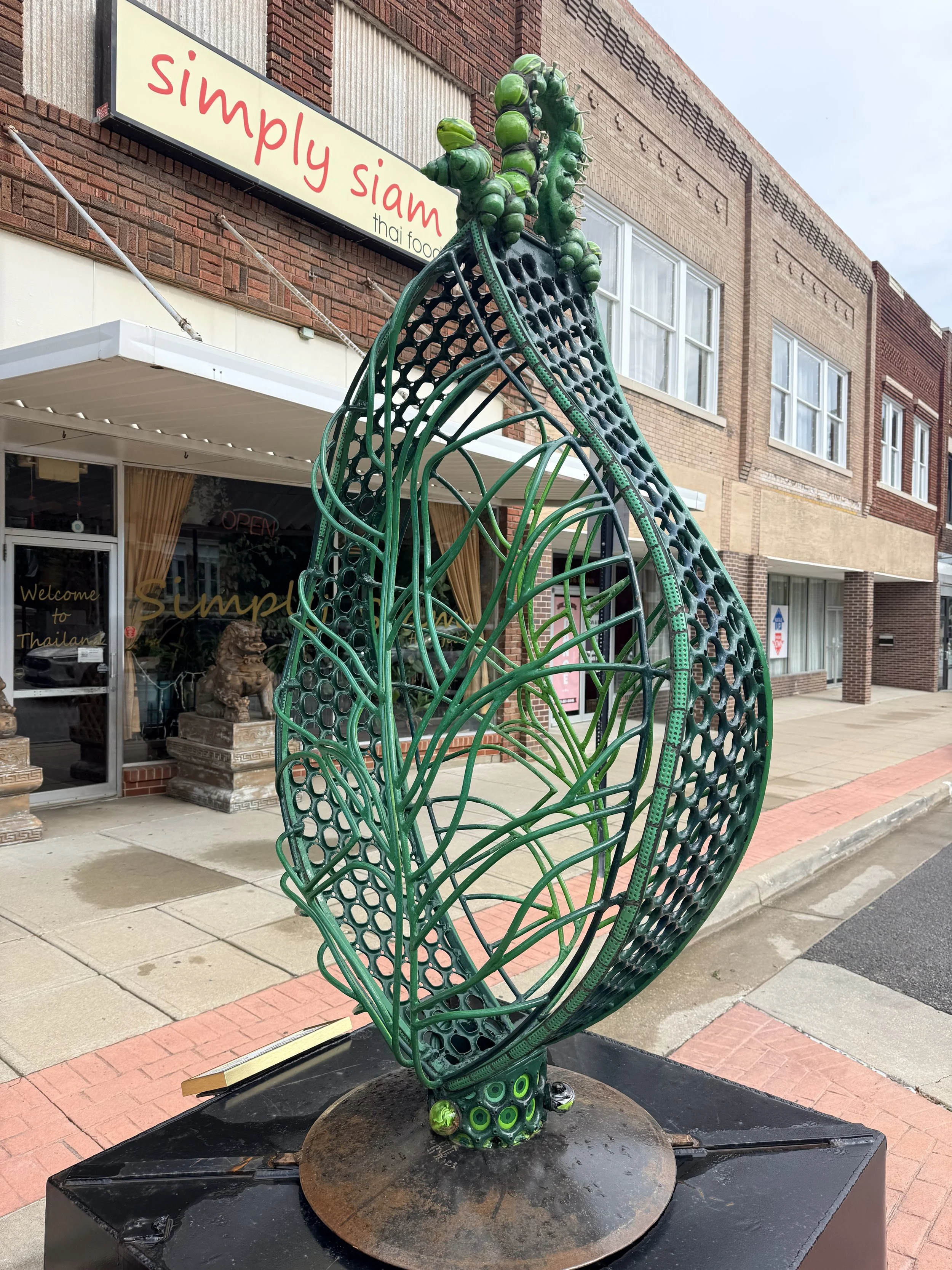 A leaf like sculpture with a bubble shaped caterpillar on top.