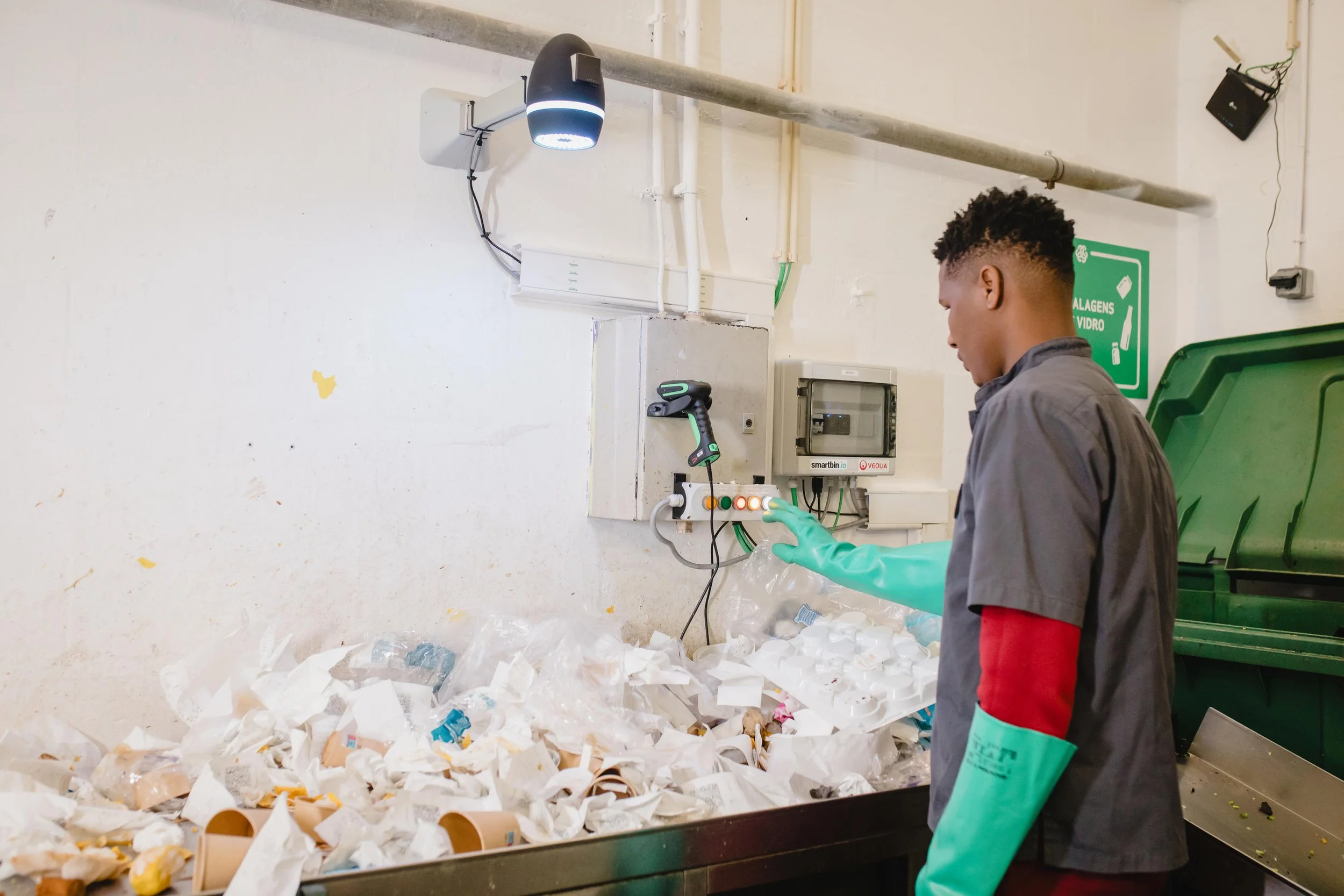 a waste sorter presses a button after using a qr code scanner to identify a bag, above an AI camera takes a picture of the waste