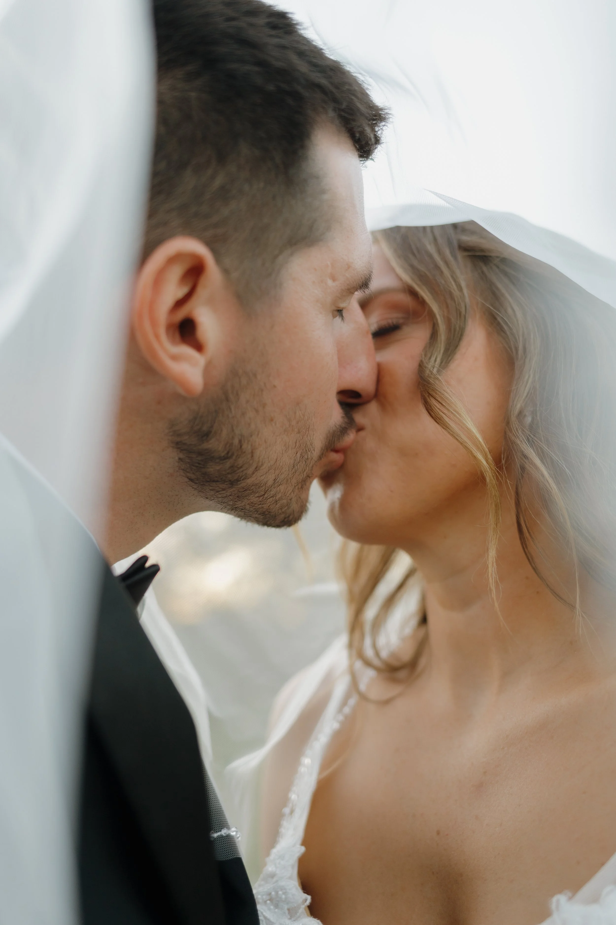 Close-up of a bride and groom sharing a kiss under a veil during their wedding.