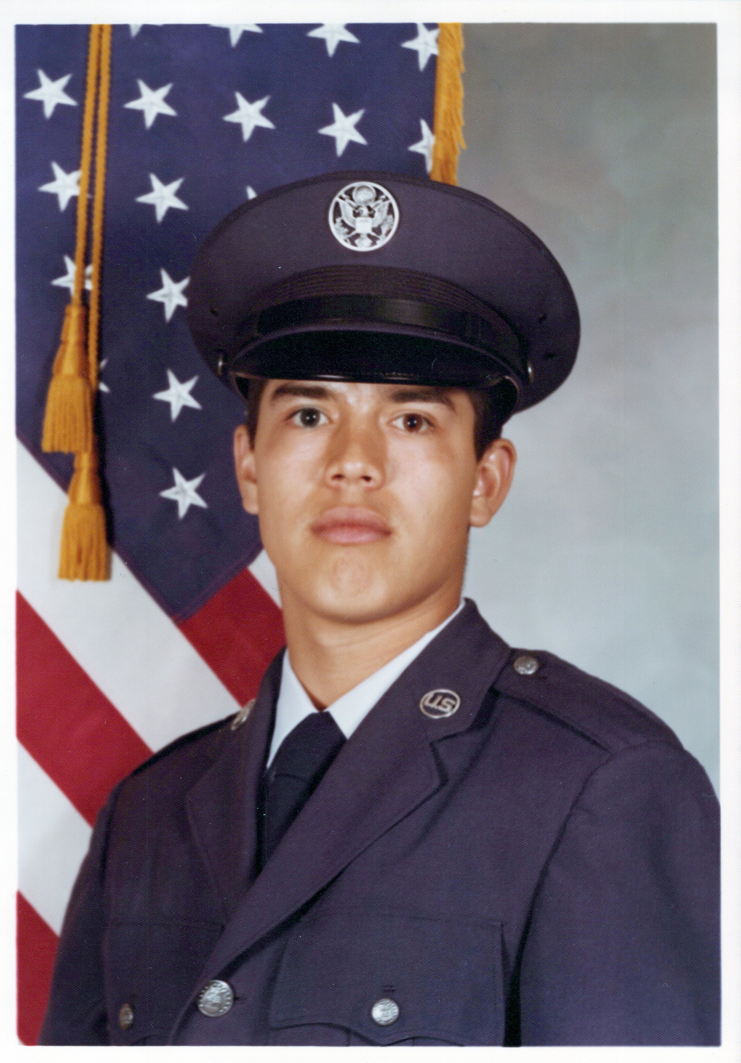 A young male U.S. Air Force officer in uniform posing in front of an American flag.