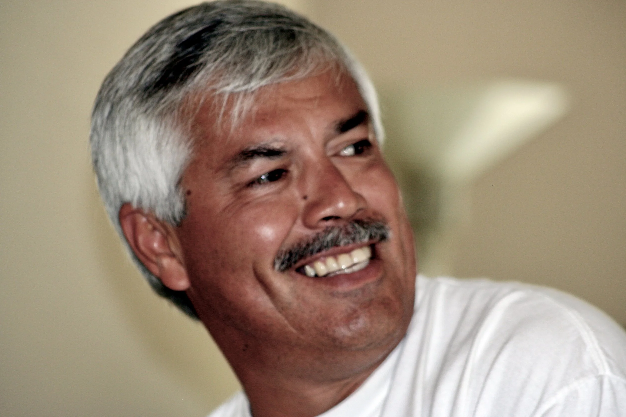 A smiling middle-aged man with gray hair and a mustache, wearing a white shirt.