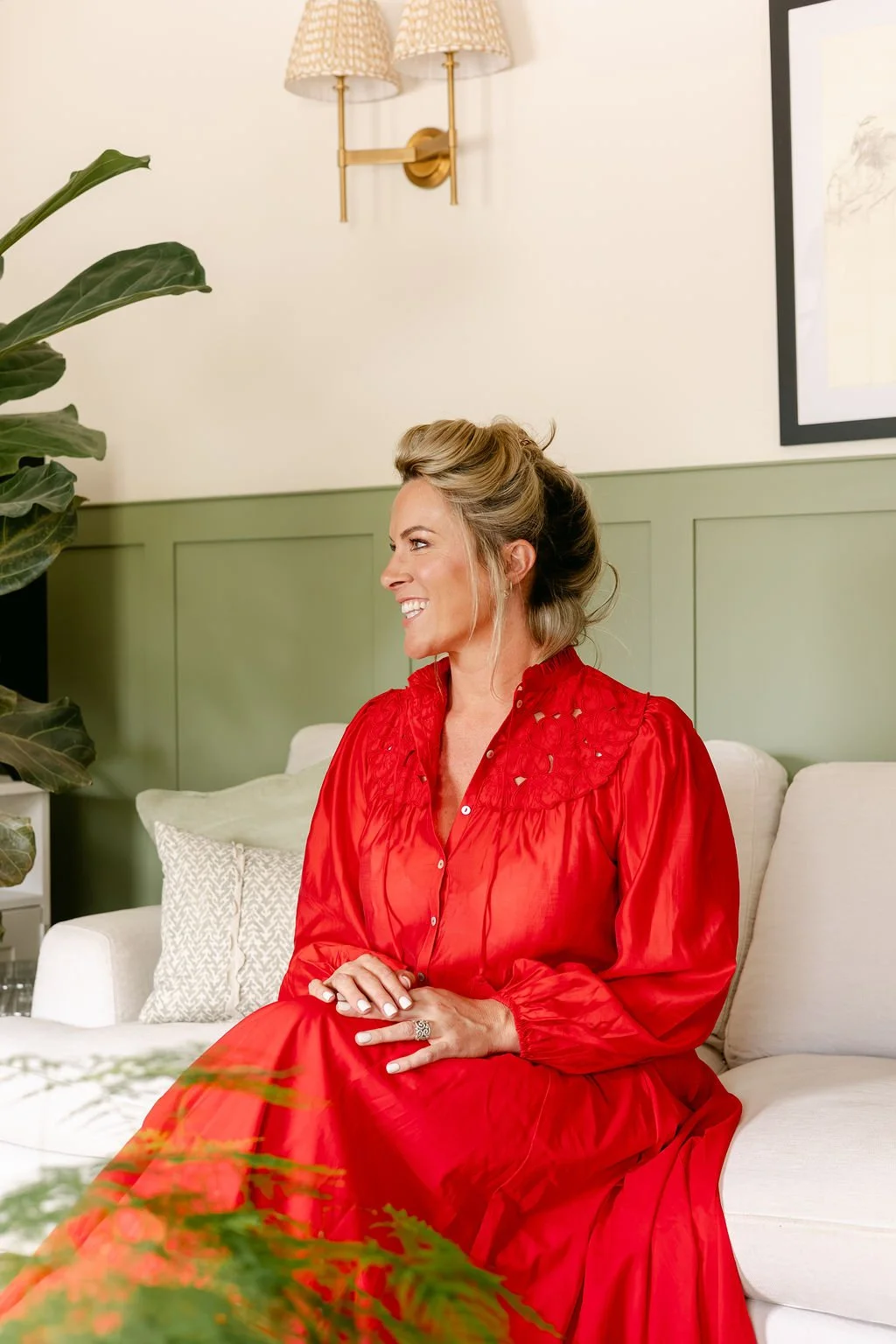 Smiling woman in a bright red dress seated on a cream sofa in a stylish living room