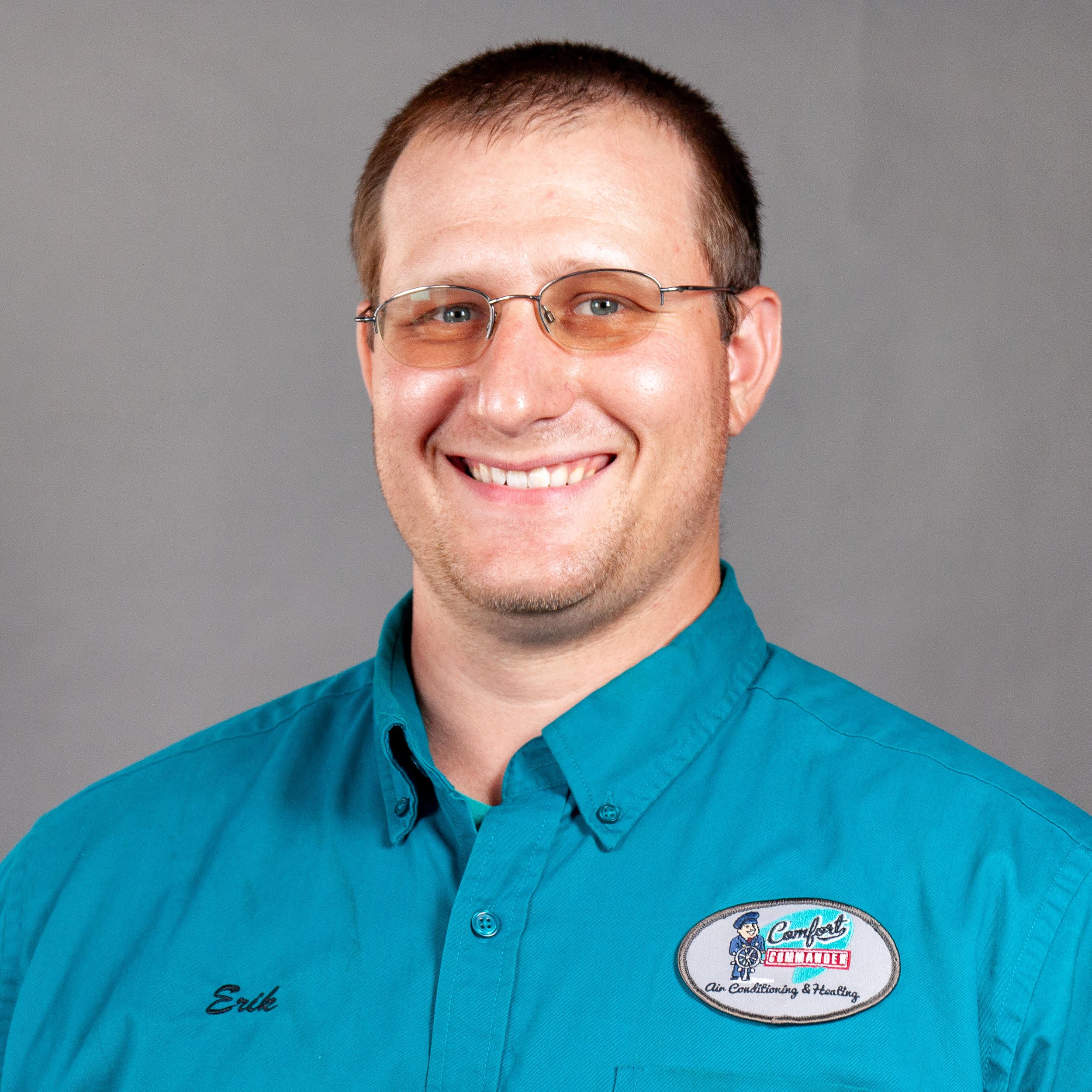 Smiling man in tinted glasses wearing a teal button 